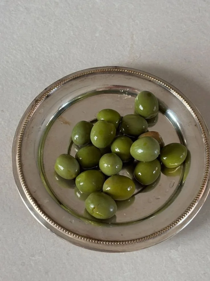 Green olives in a silver dish.