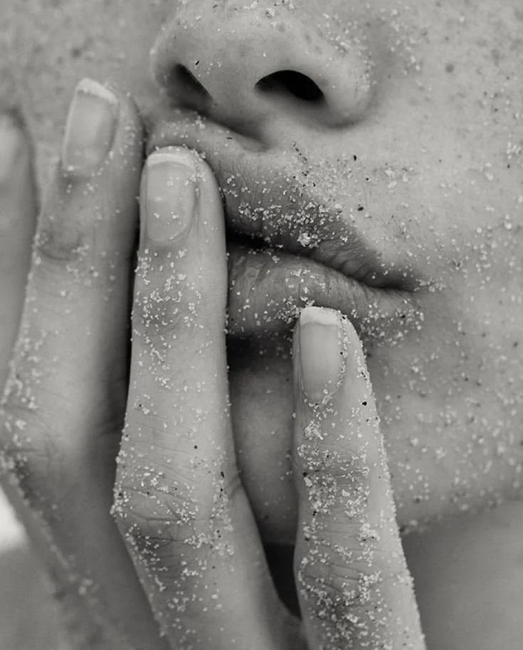 Close-up of a person's face with sand on their hand, lips, and nose, fingers touching lips, black and white photo.