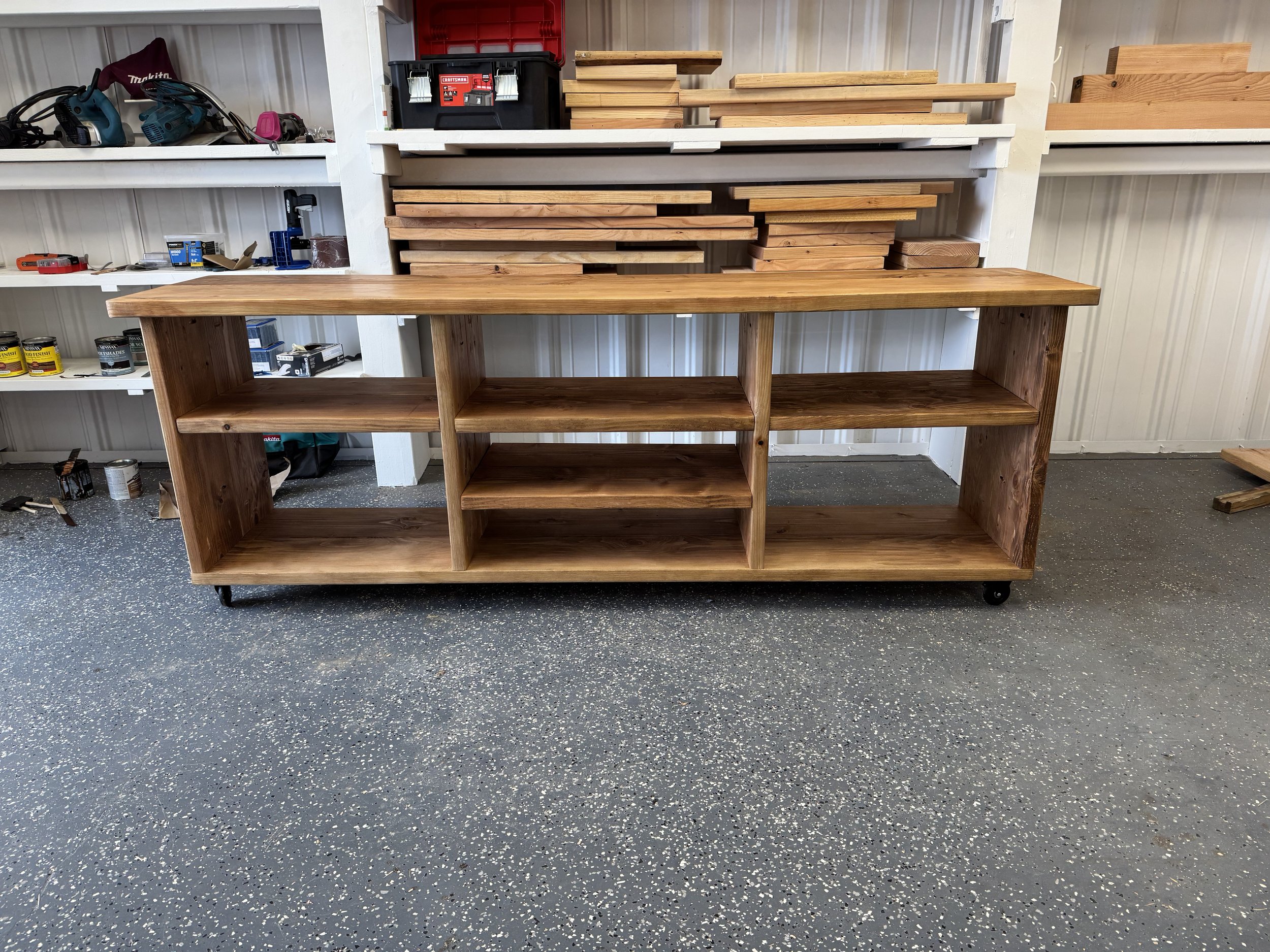 Wooden workbench in a workshop with shelves filled with various woodworking tools and materials.