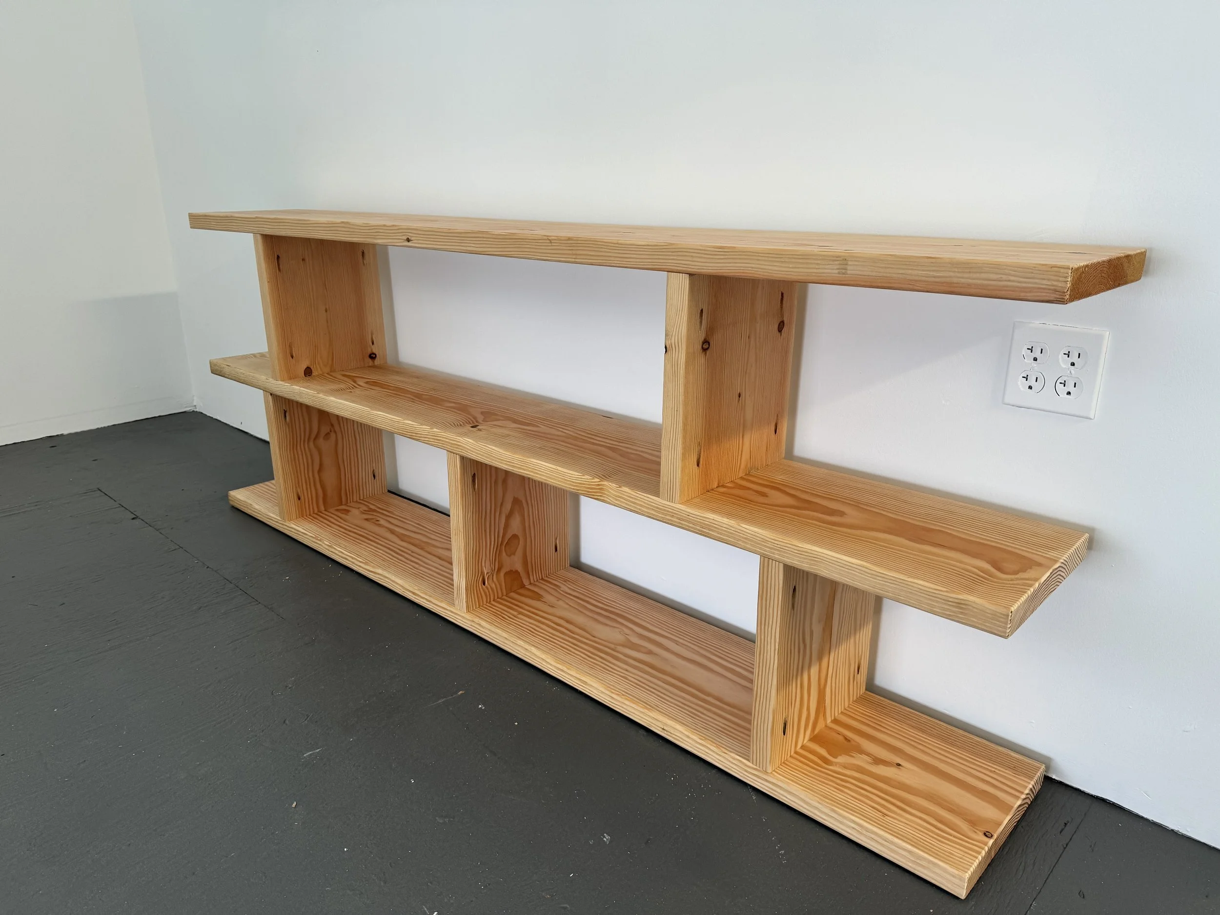 A wooden shelf with three levels against a white wall, plugged into an electrical outlet.