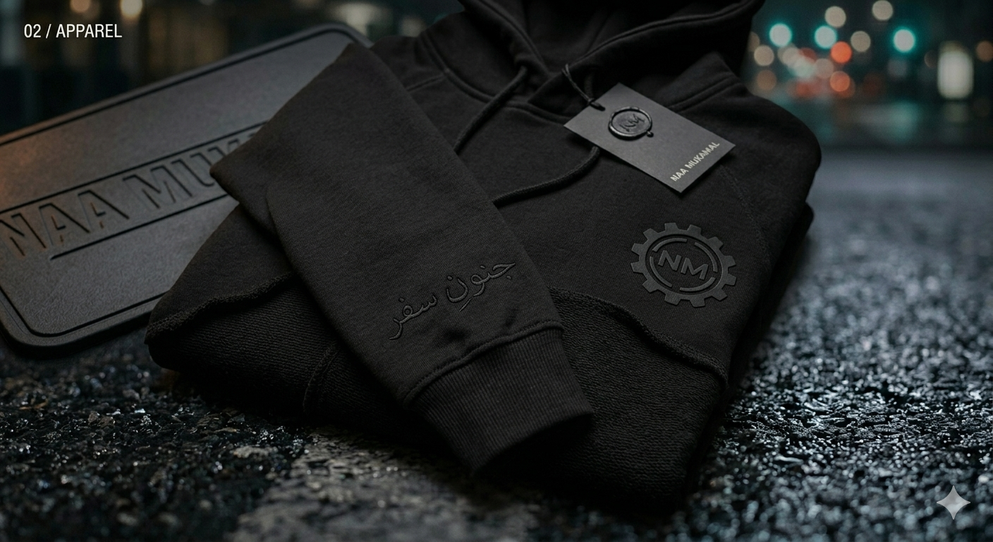 Black hoodie with a logo and Arabic script, folded on a textured surface at night, with city lights blurred in the background.