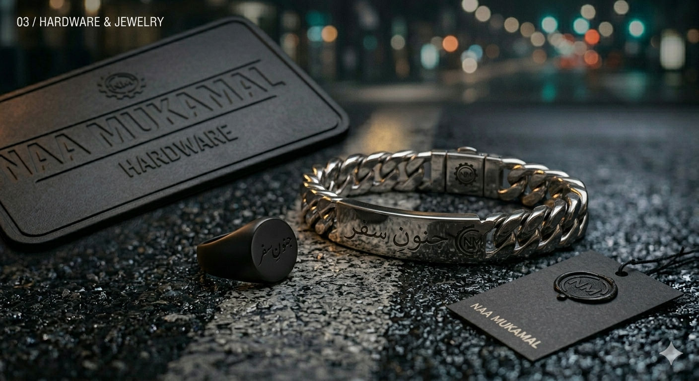 A jewelry and accessory display featuring a black case labeled "NAA MUKAMAL HARDWARE," a silver chain bracelet with Arabic inscriptions, a black earring with Arabic writing, and a black tag with the NAA MUKAMAL logo, all arranged on a textured black surface with a blurred city street background.