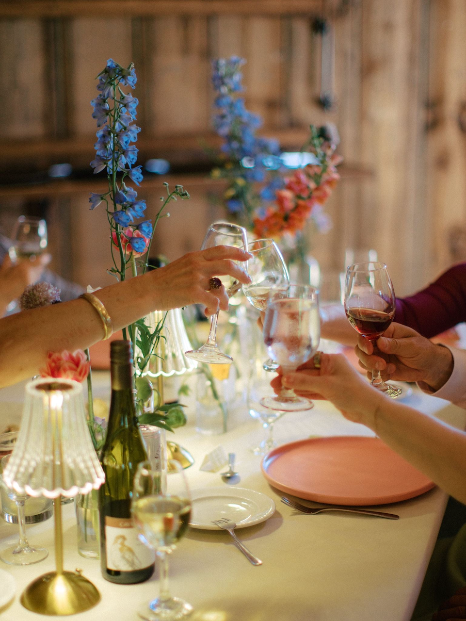 People raising wine glasses in a toast at a dinner table decorated with flowers and candles.