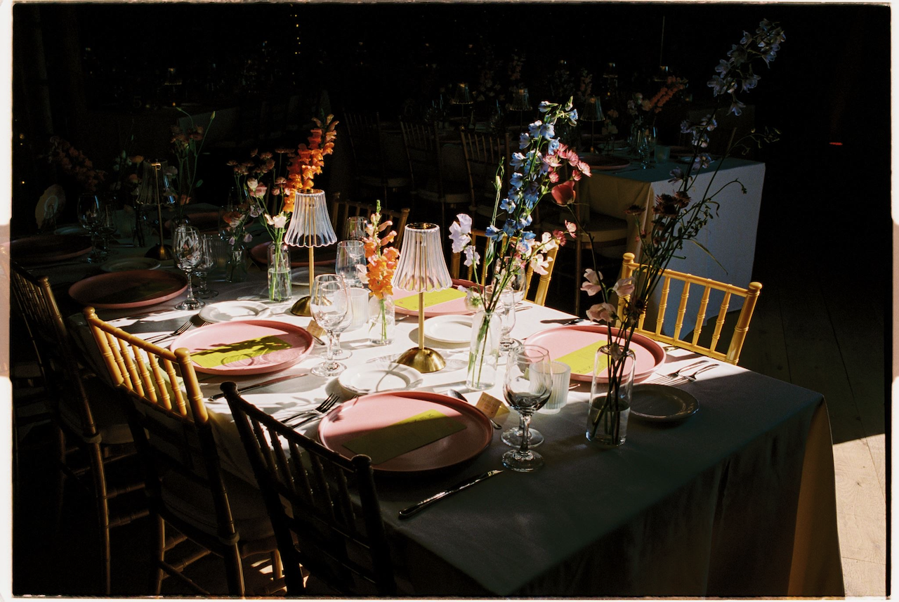 Elegant dining table set with pink plates, wine glasses, candles, and floral centerpieces in sunlight