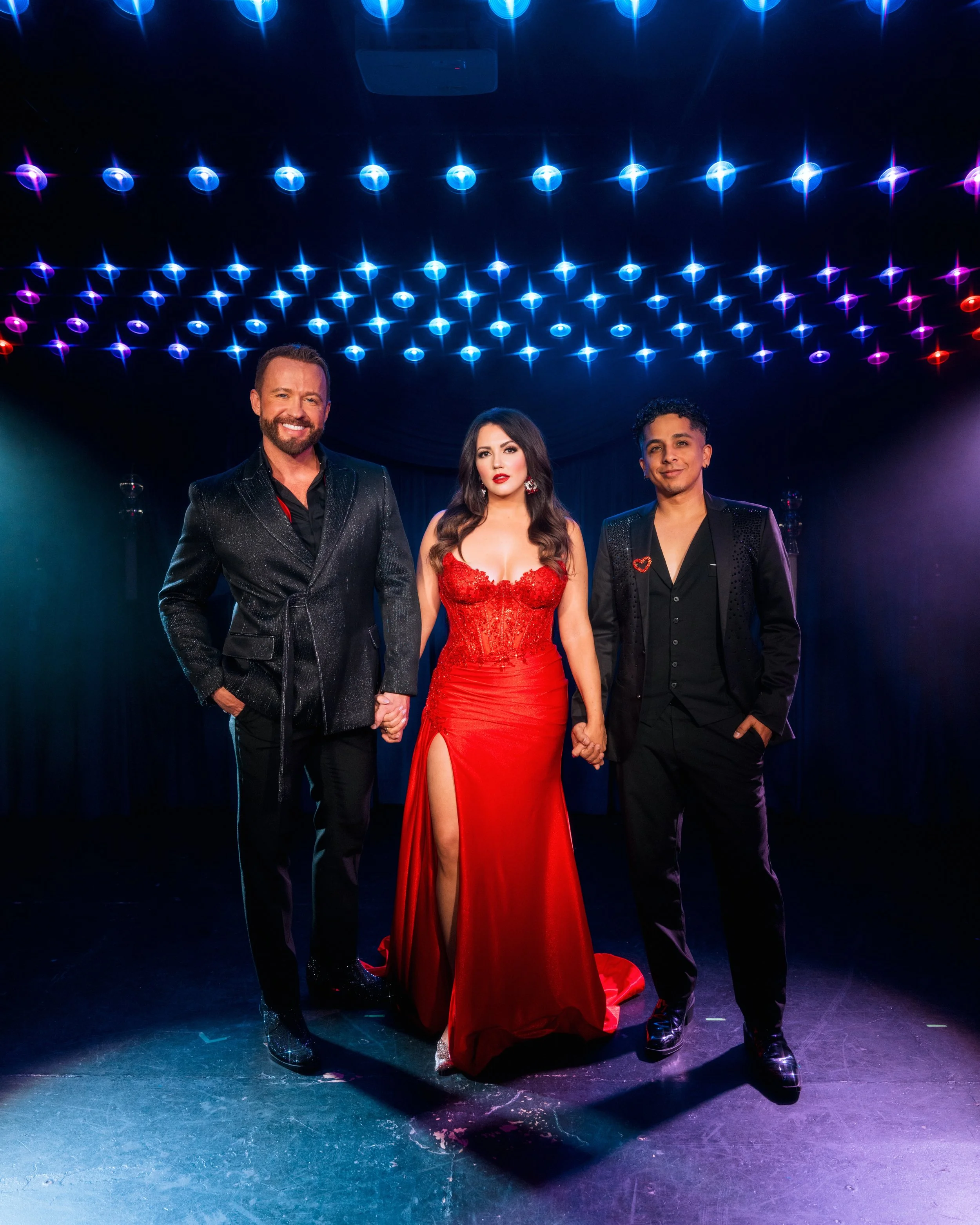 Triple Threat (trio vocal group) consisting of Marty Thomas, Rachel Potter, and Omar Cardona. The woman is wearing a red gown while the two men on either side are in black suits. theatrical or entertainment event.