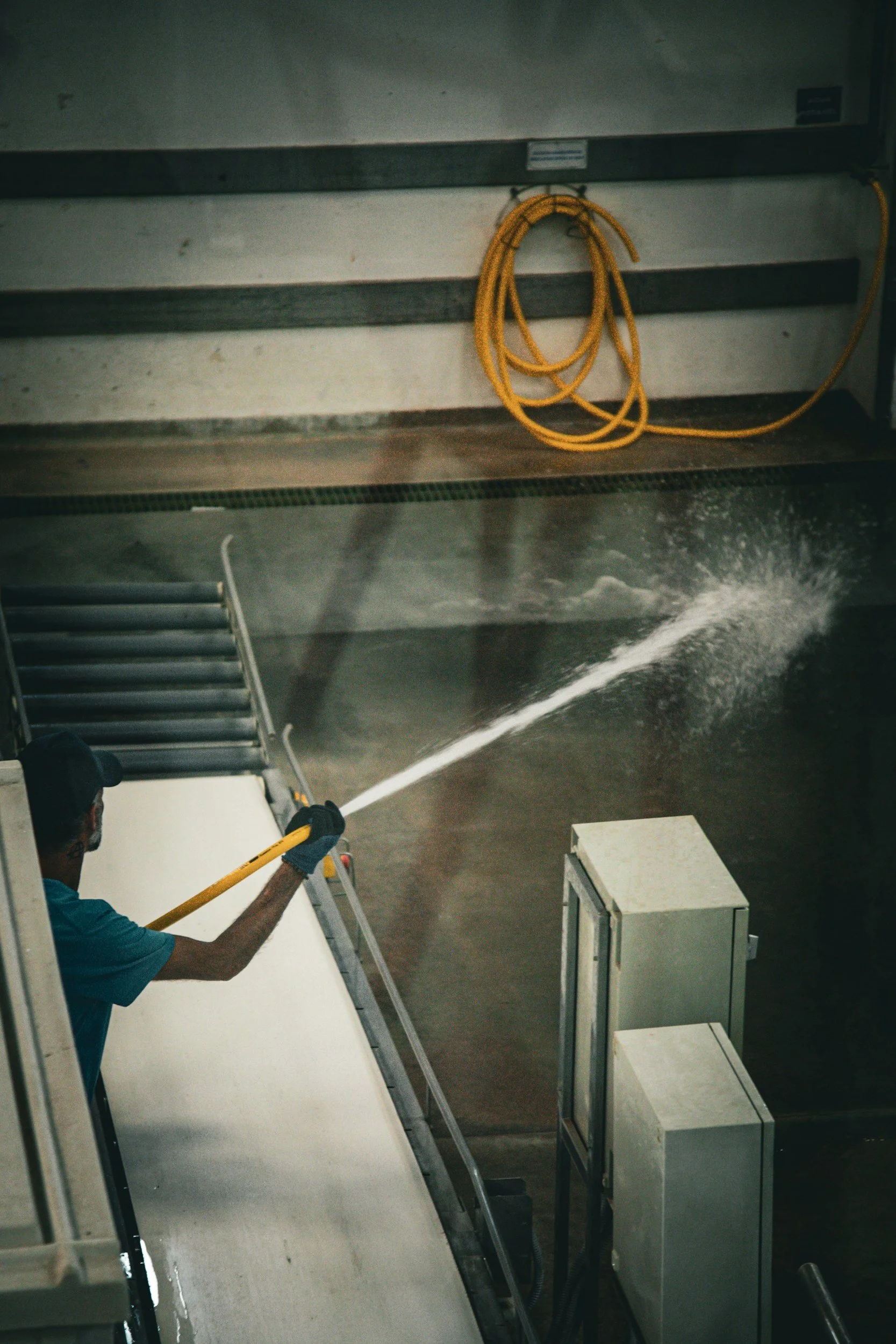 Person spraying disinfectant onto an escalator handrail at an indoor facility.
