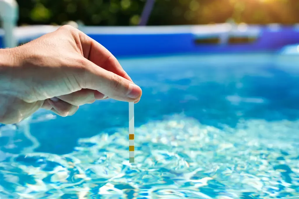 A person holding a water test strip above a swimming pool.