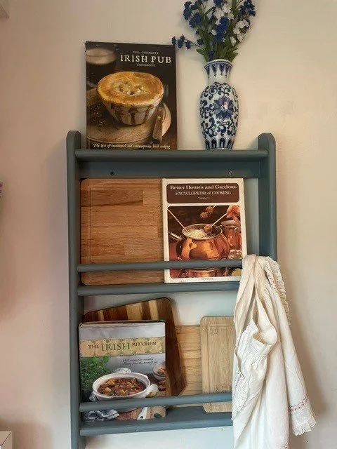 A bookshelf with a floral vase, several cookbooks, and a white towel hanging on the side.