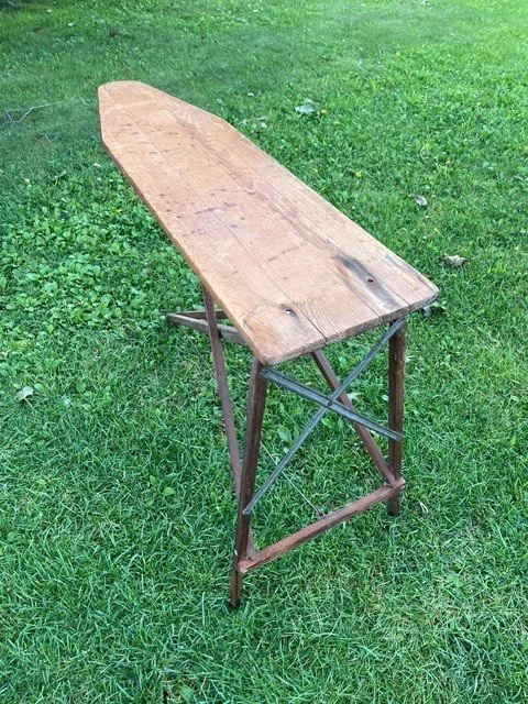 A wooden ironing board with metal legs placed on a grassy lawn.