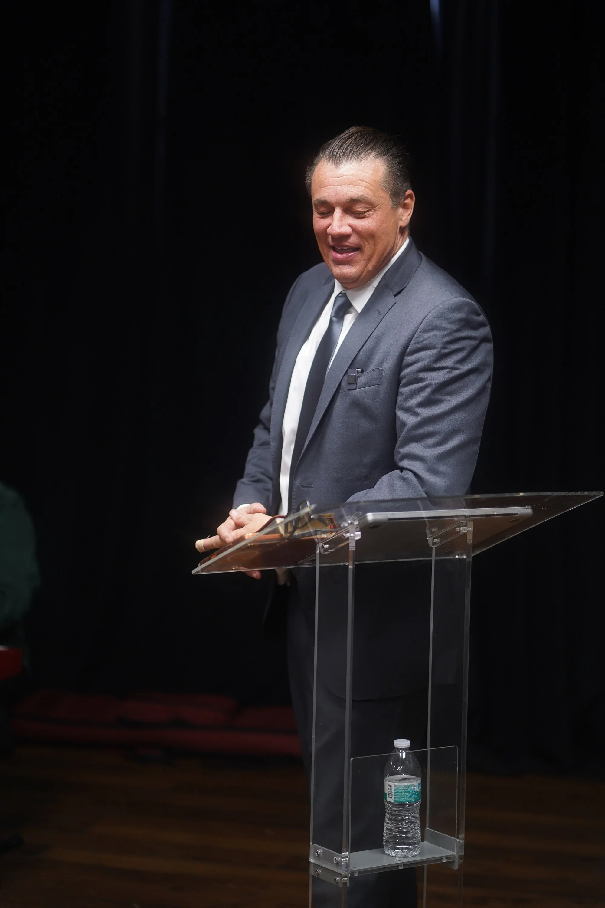 A man in a suit standing behind a clear podium preaching at at Acts Church Hollywood.