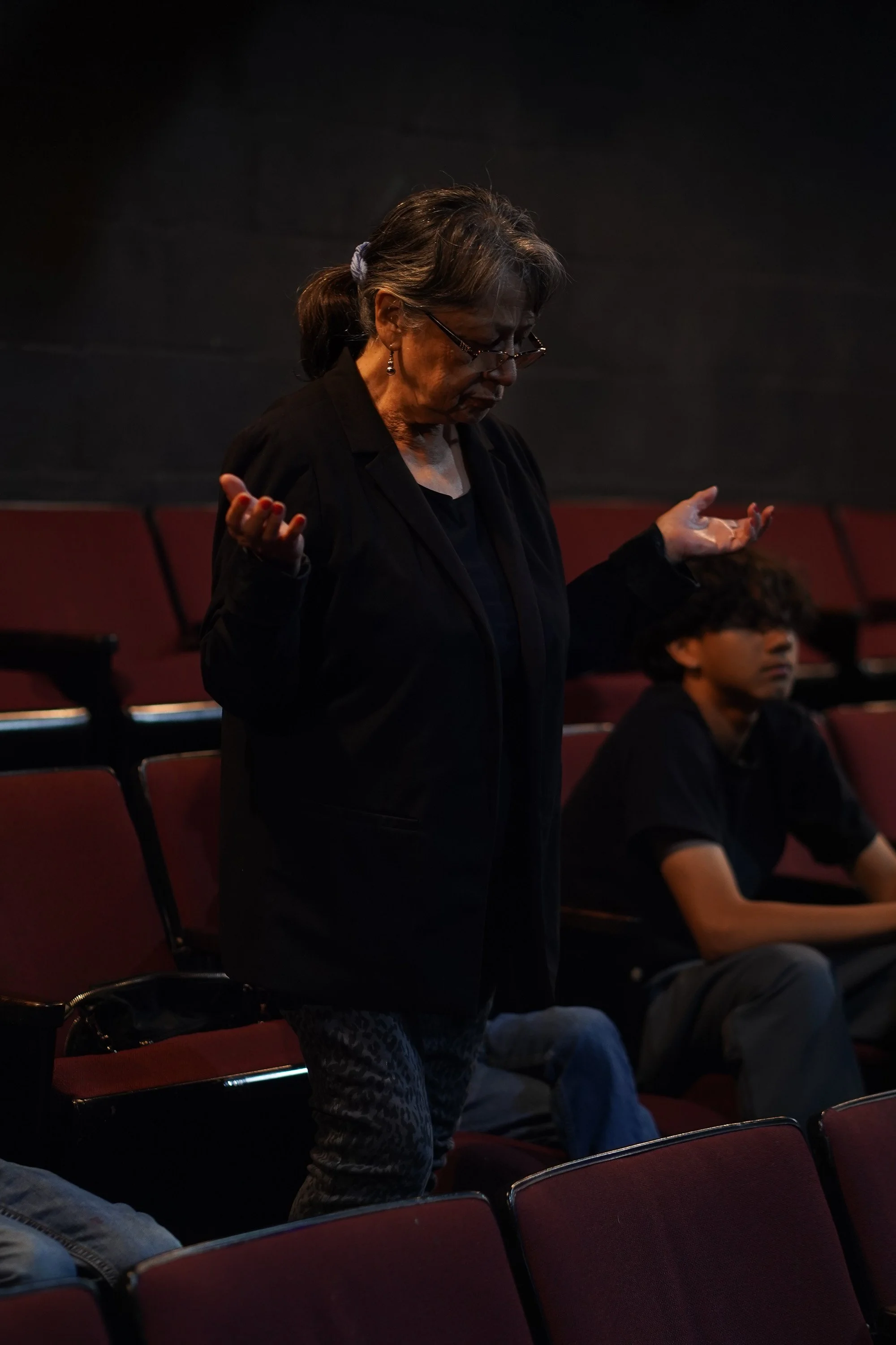 An elderly woman lifting up her hands in prayer while standing in between theater seats at Acts Church Hollywood