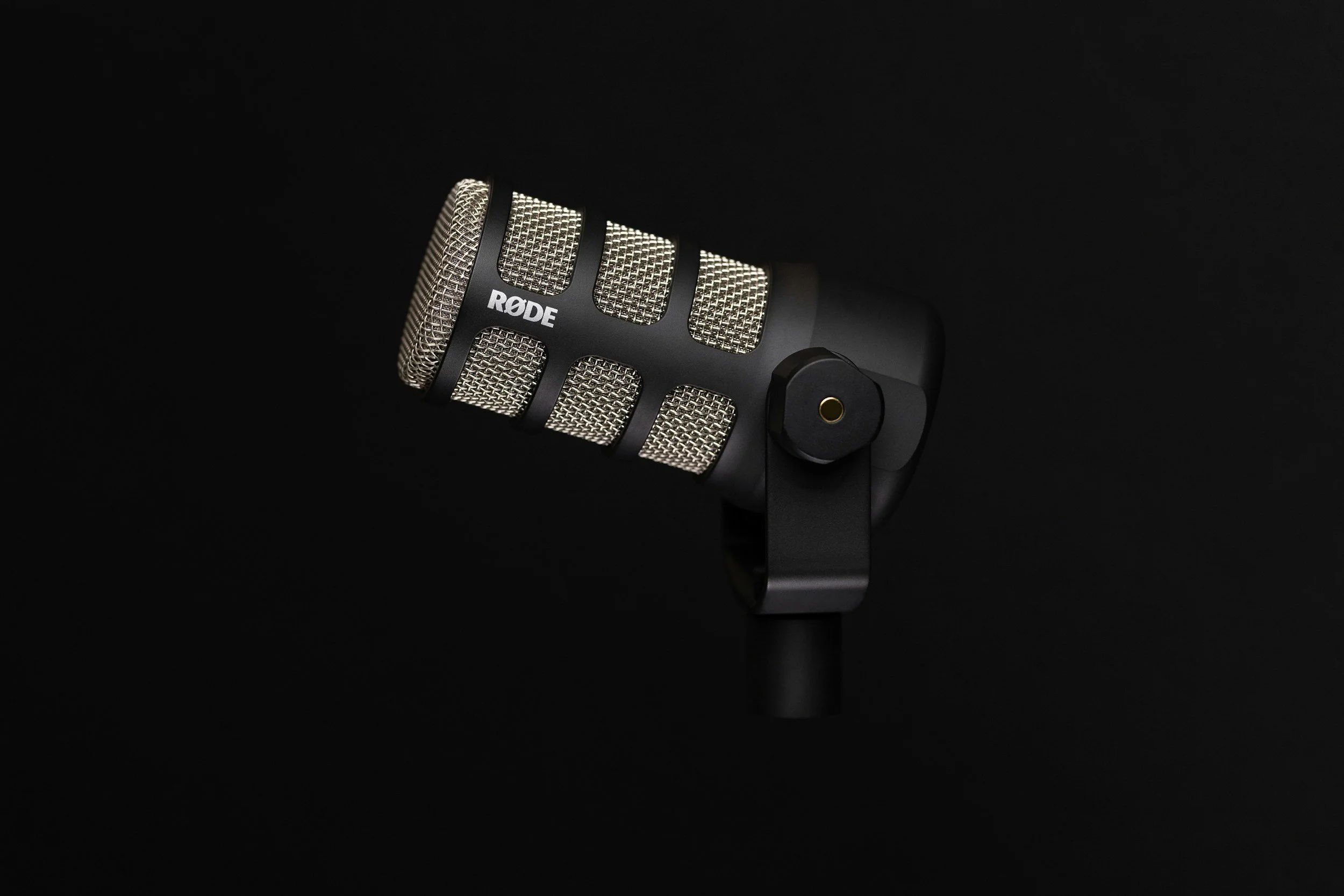Close-up of a Rode condenser microphone with a metal mesh grille and black body, against a dark background.