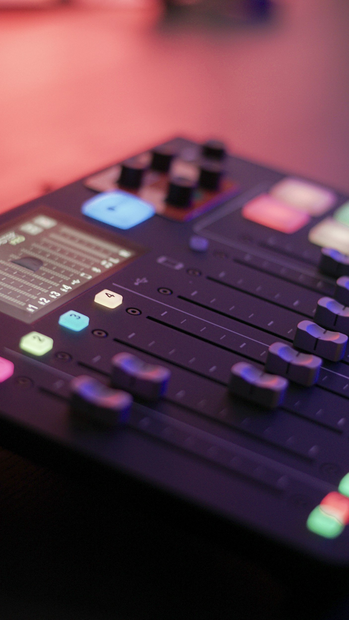 Close-up of a digital audio mixing console with illuminated buttons and sliders, used in sound production.