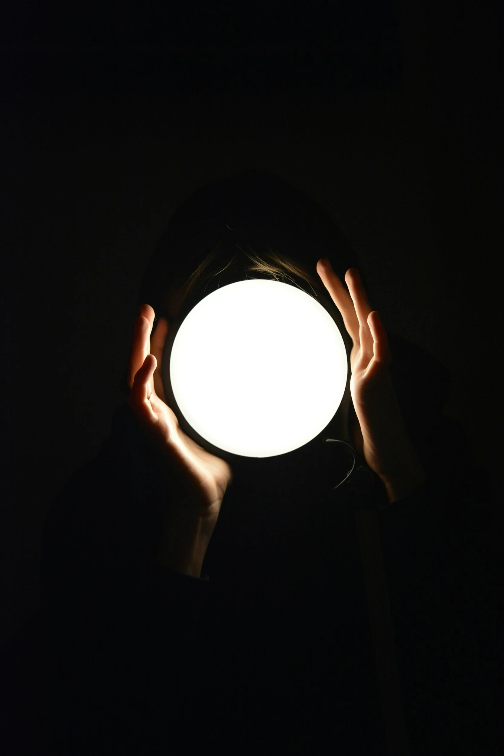 Person holding a bright, round light source in a dark environment, with hands around the light.