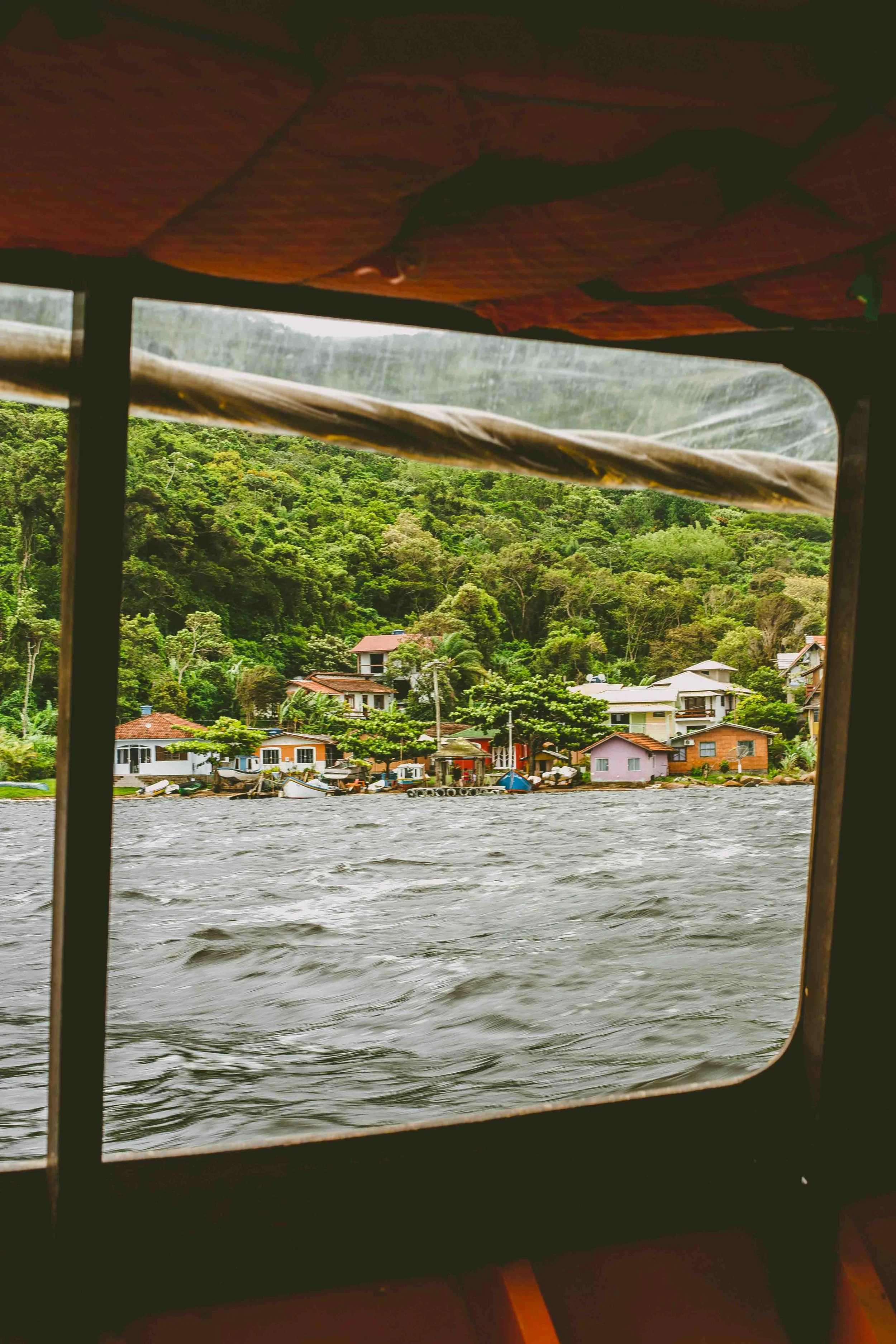 View from a boat window showing a small residential neighborhood along a body of water surrounded by lush green trees.