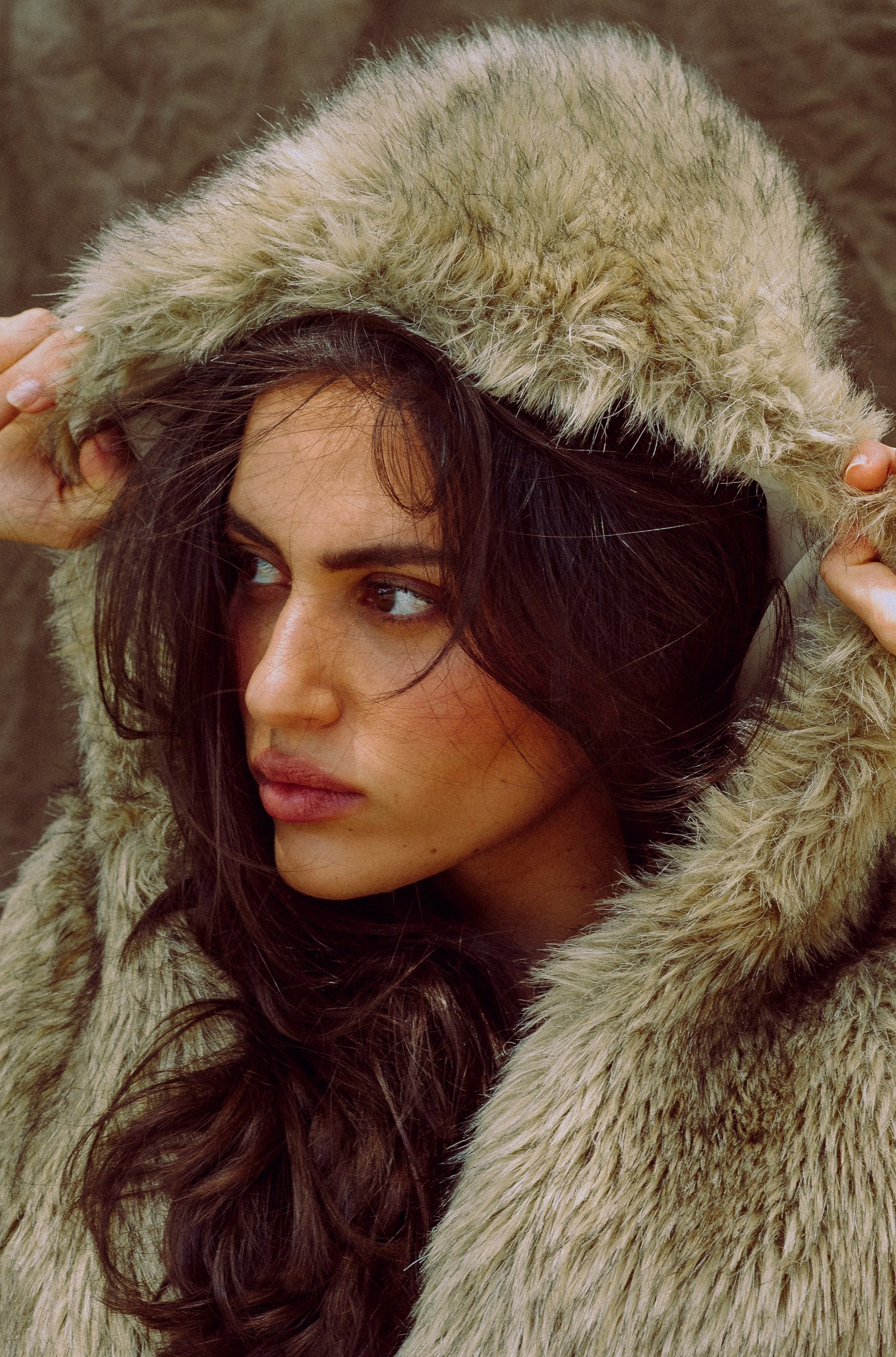 A woman with long dark hair wearing a fur-lined hooded coat, looking to the side.