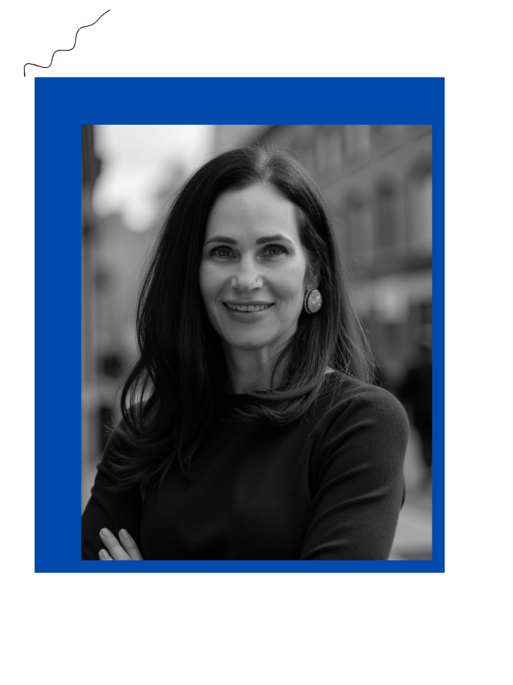Black and white portrait of a woman with dark hair, smiling and wearing earrings, outdoors on a city street.