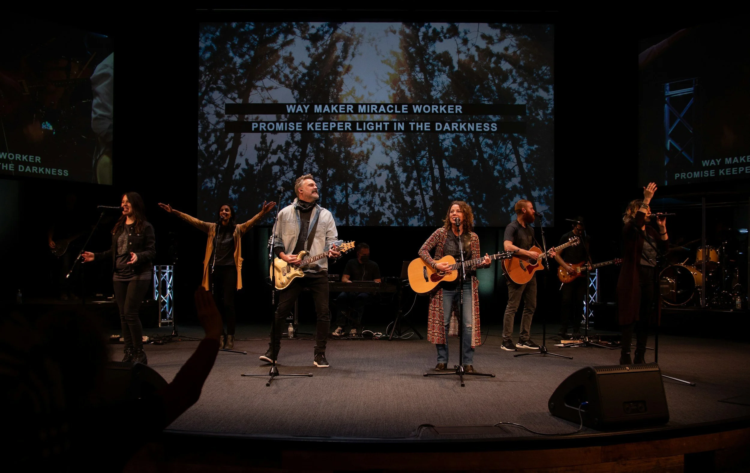 Worship band leading worship with guitars and microphones on stage.