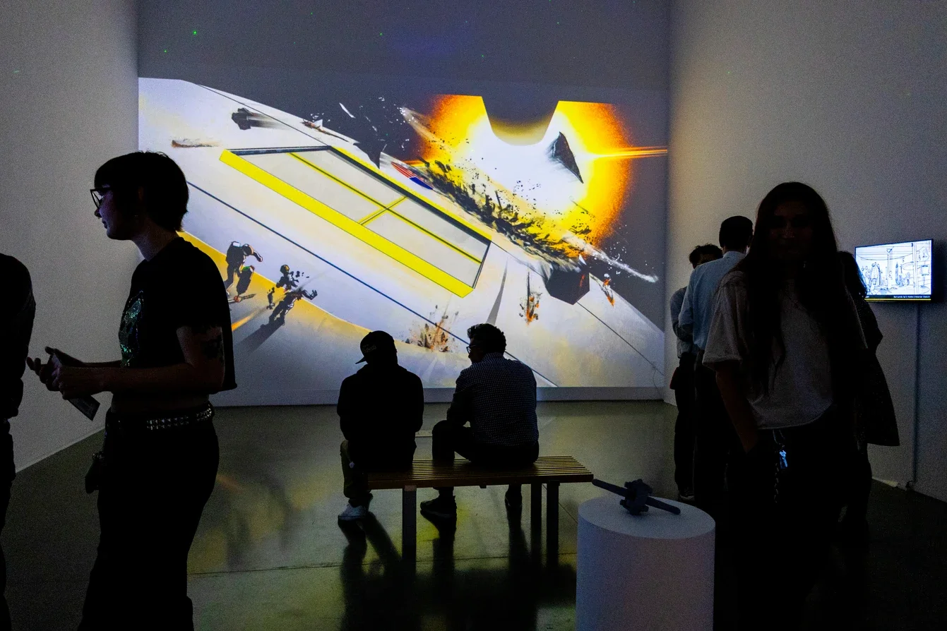 People in a dark gallery viewing a large digital art projection on the wall with abstract, colorful visuals.