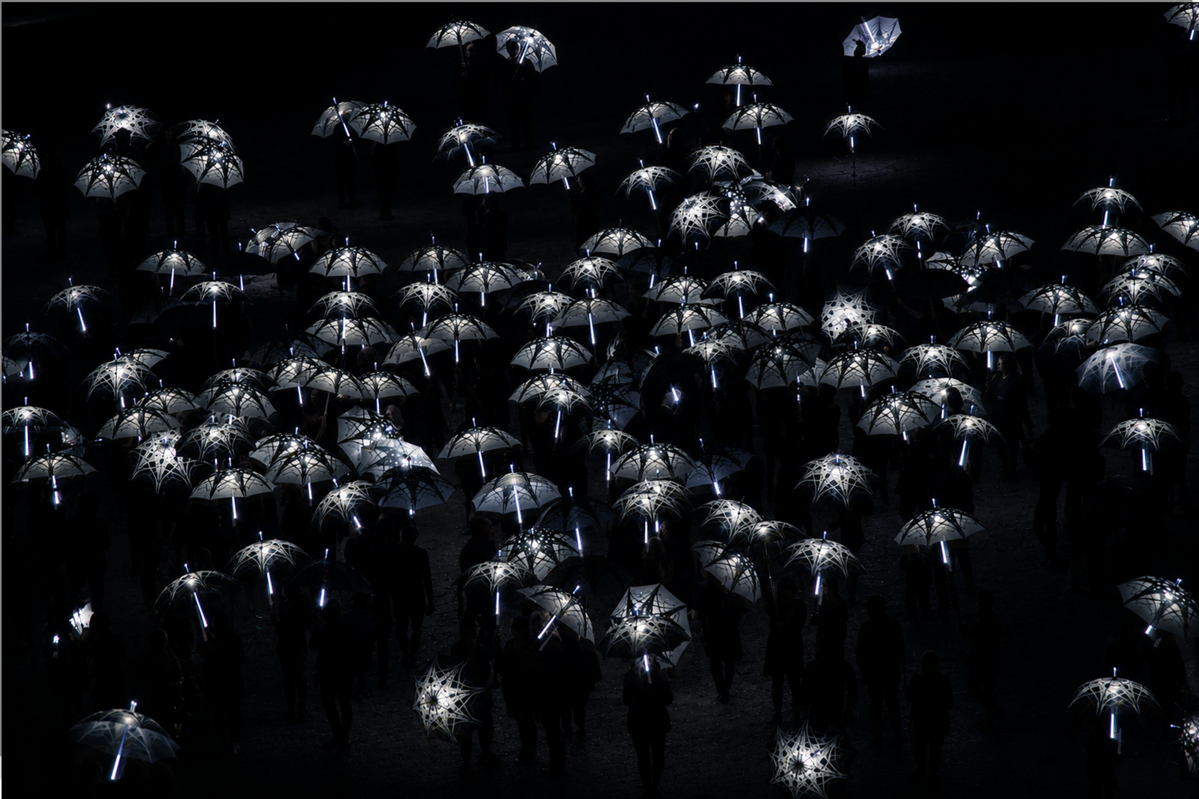 A large group of people holding illuminated umbrellas in a dark setting.