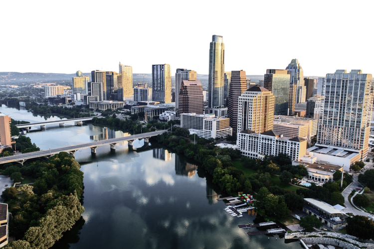 Aerial view of a city skyline with a river flowing through downtown, featuring tall skyscrapers, bridges, and green parks.