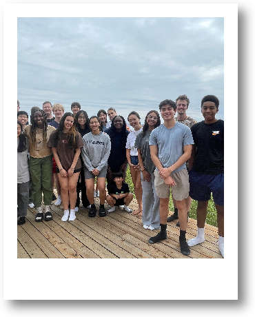 Group of young people standing on a wooden deck outdoors, under a cloudy sky.