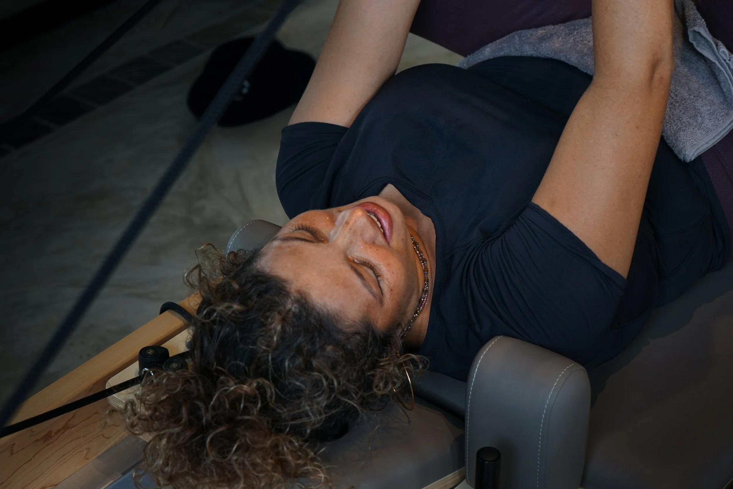 A woman with curly hair and lying on a reformer pilates machine