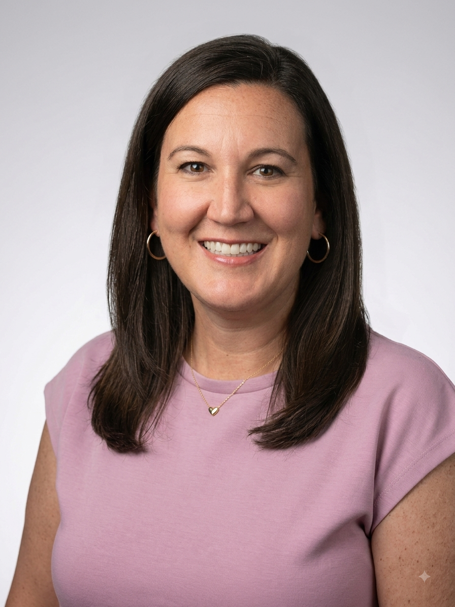 Headshot of a smiling woman with dark brown hair, wearing hoop earrings, a pink top, and a gold heart necklace against a plain light background.