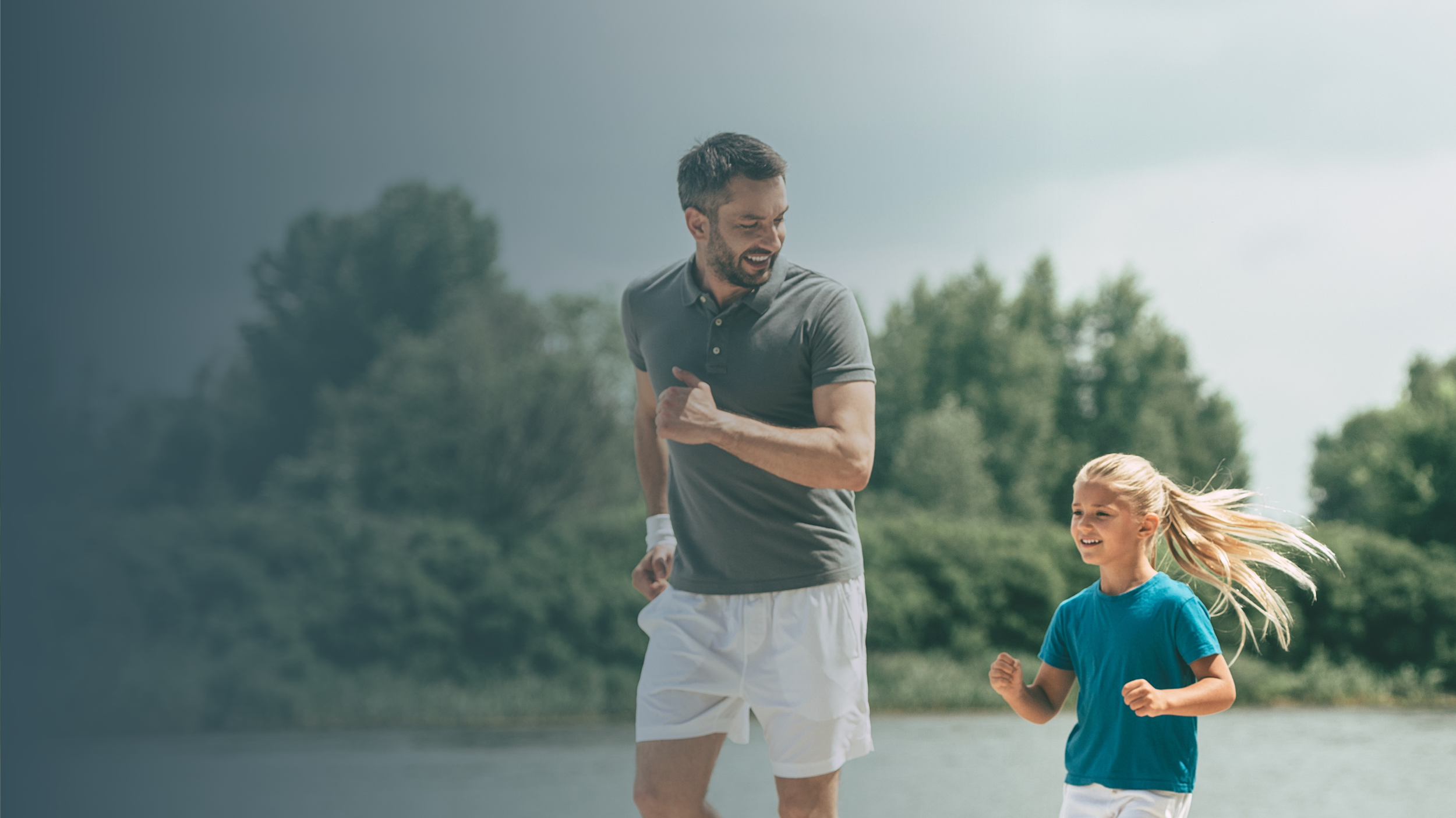 A man and a young girl are running outdoors in a park, smiling and enjoying their activity.