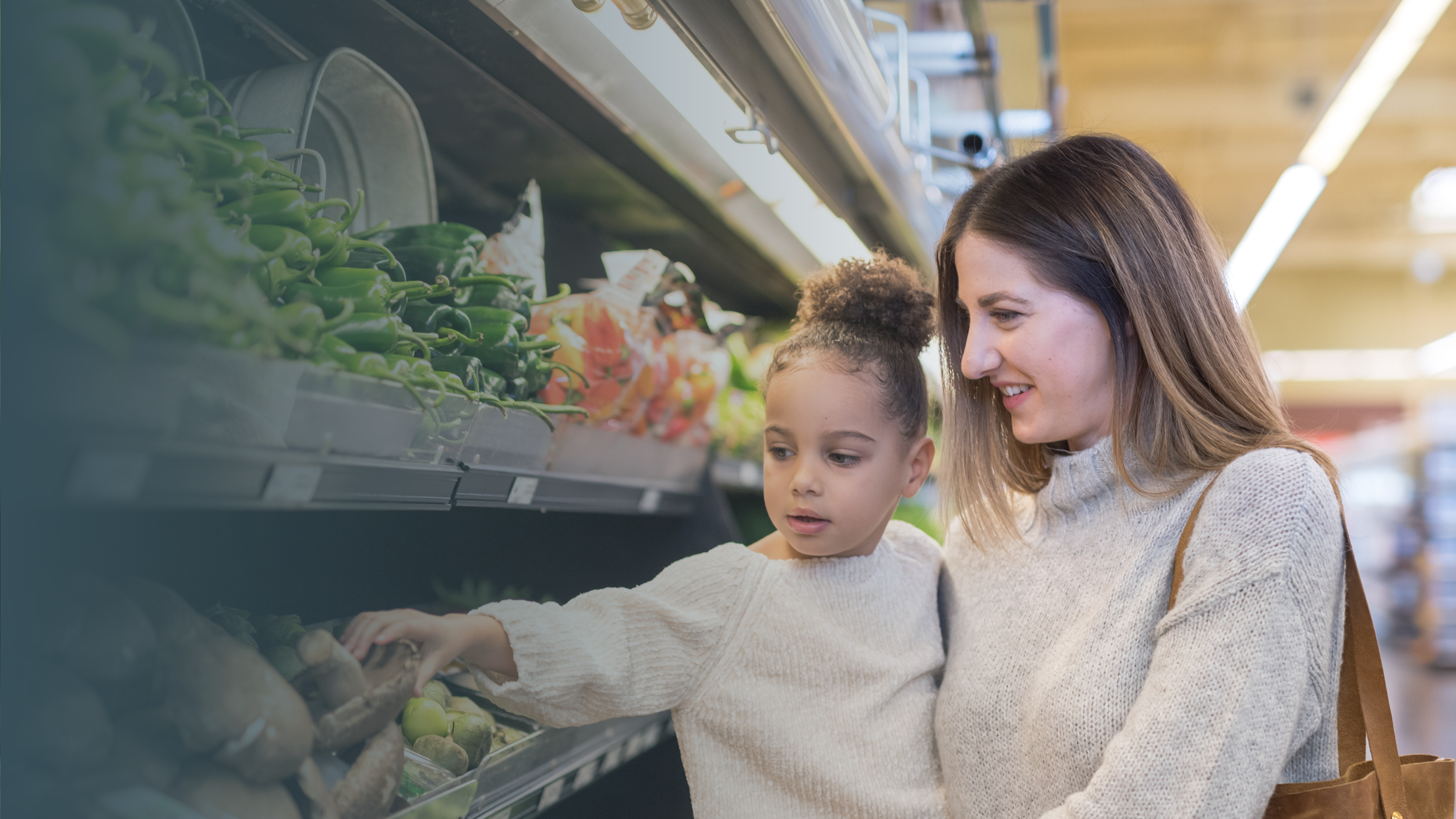 A woman and a young girl shopping for vegetables in a grocery store aisle.