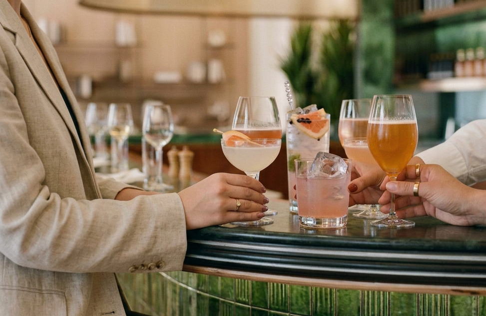 People holding and serving various colorful cocktails at a bar.