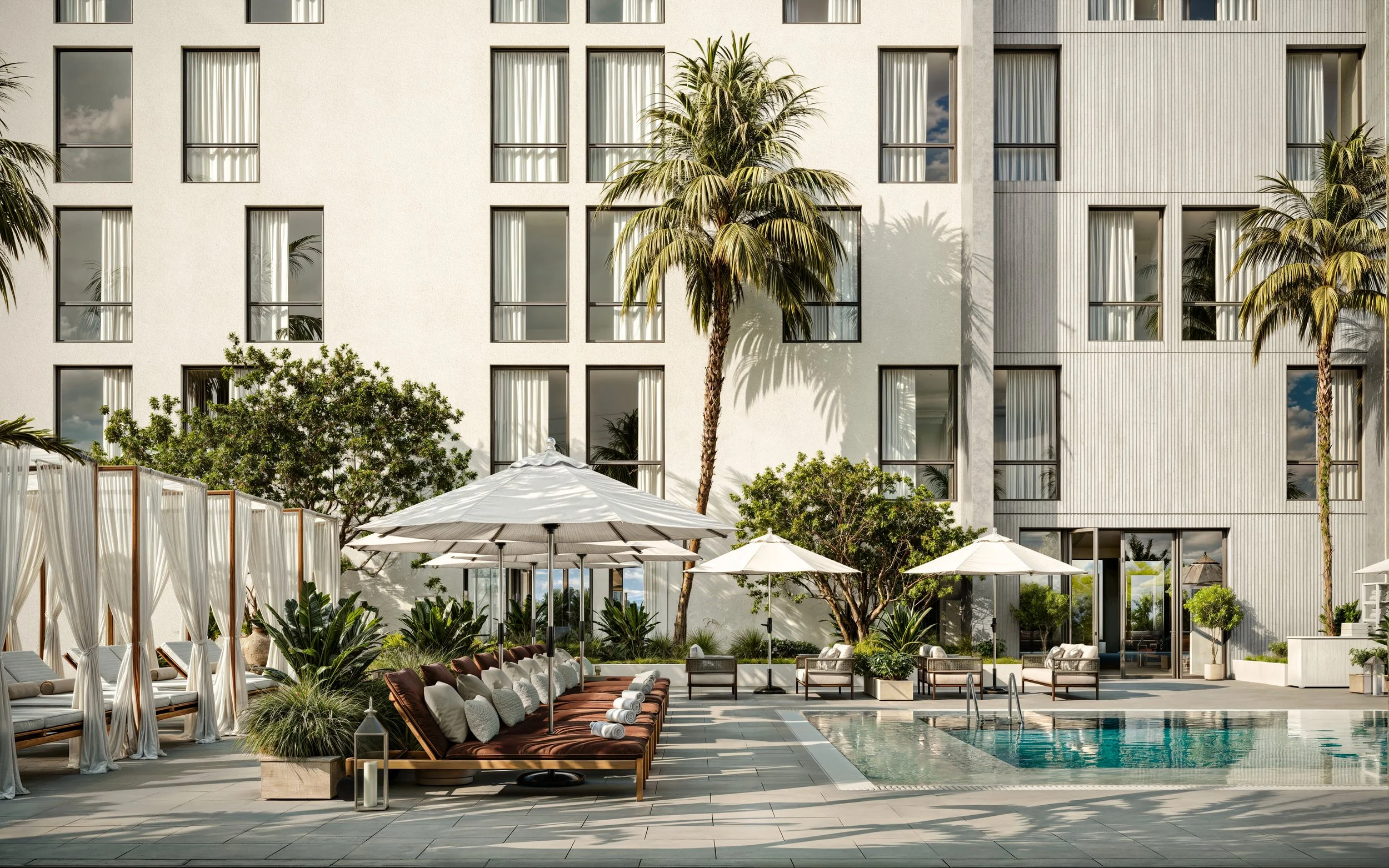 An outdoor pool area in front of a modern building with multiple windows, surrounded by lounge chairs, umbrellas, and lush greenery, including palm trees.