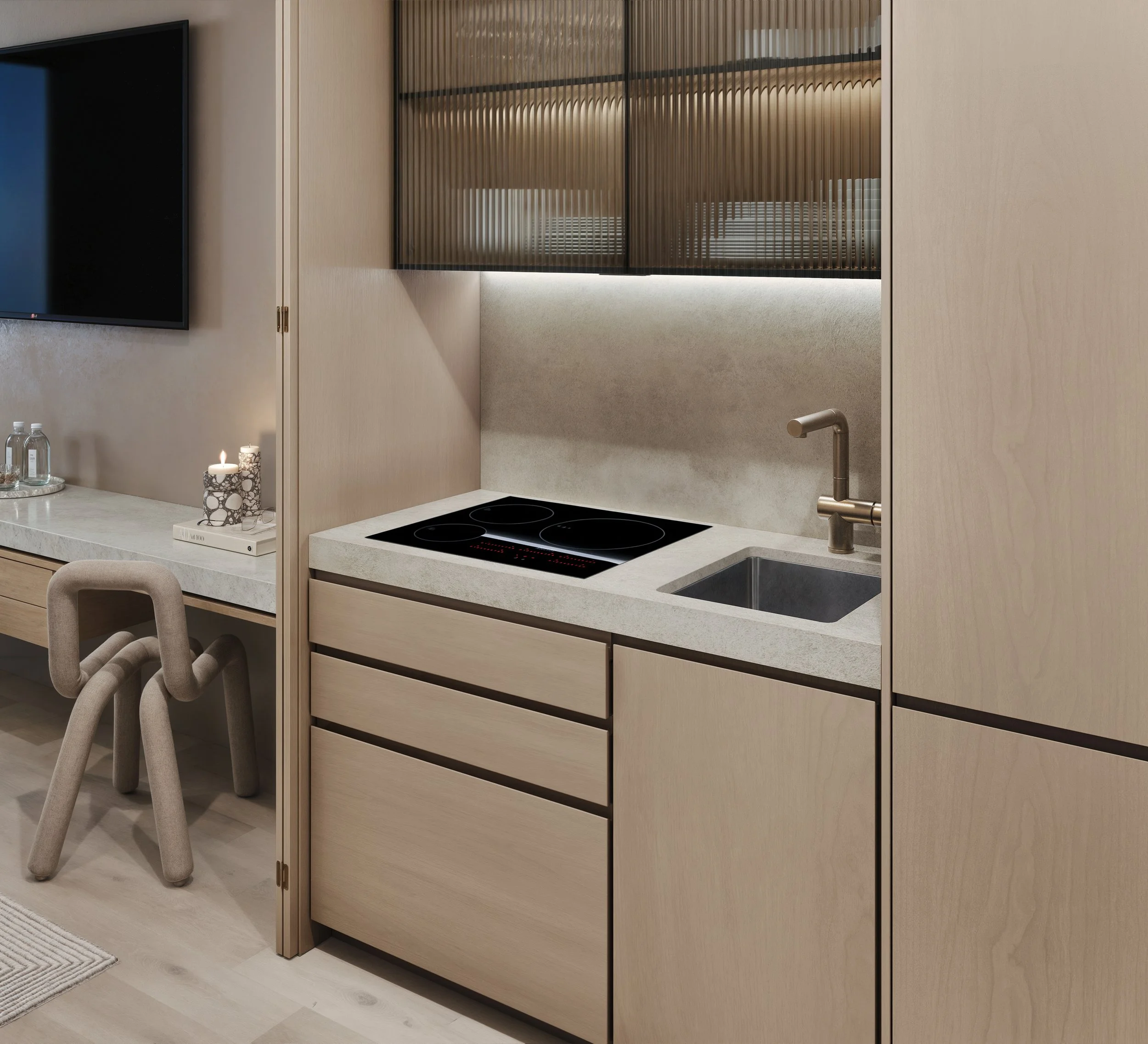 Modern kitchen with beige cabinets, black stovetop, and a gold backsplash with vertical ridges. A black wall-mounted television is visible on the left, with a corner of a dining chair at the bottom.
