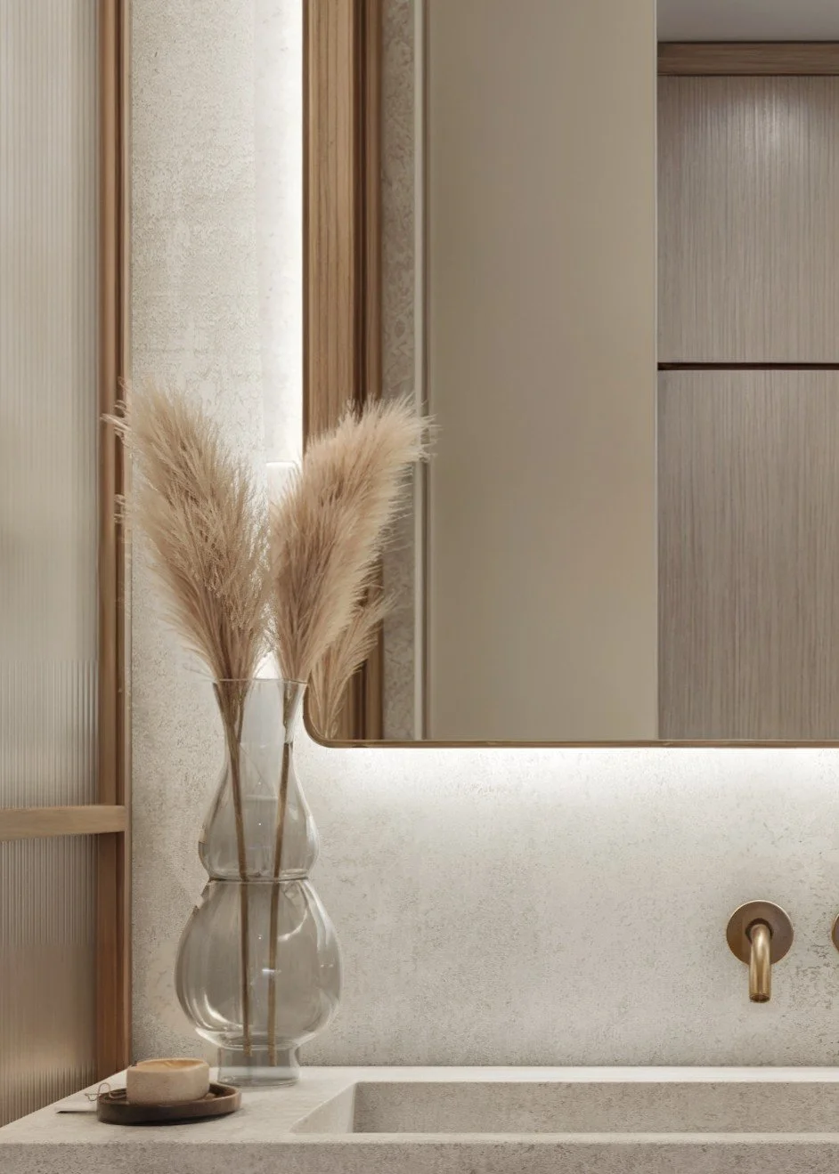 Decorative beige pampas grass in a clear glass vase on a white bathroom countertop with a mirror above, with neutral-colored walls and cabinets in the background.