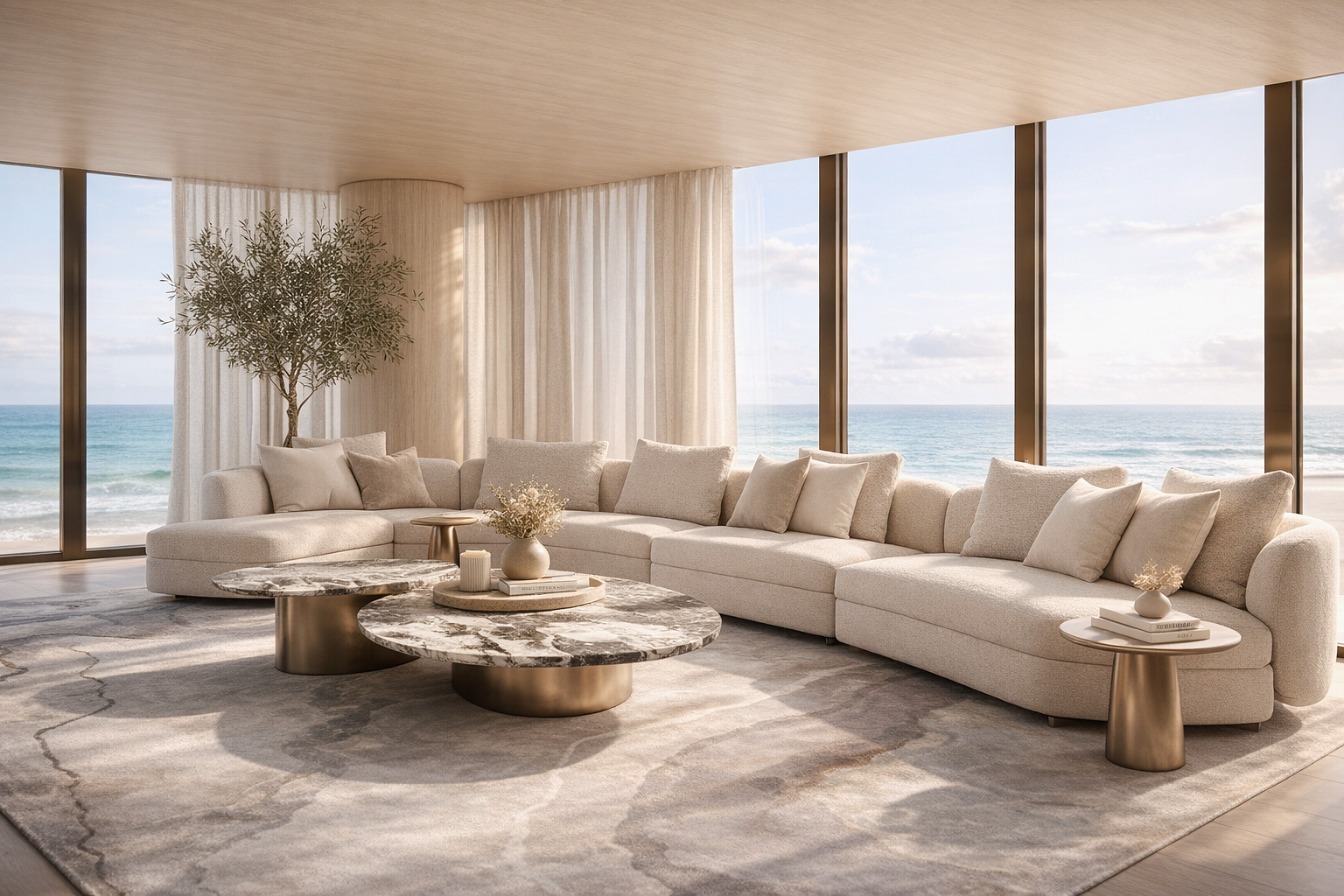 Elegant beachfront living room with a large cream sectional sofa, two marble-top coffee tables, beige pillows, a small side table with books and flowers, a potted tree, and floor-to-ceiling windows showing the ocean and sky outside.