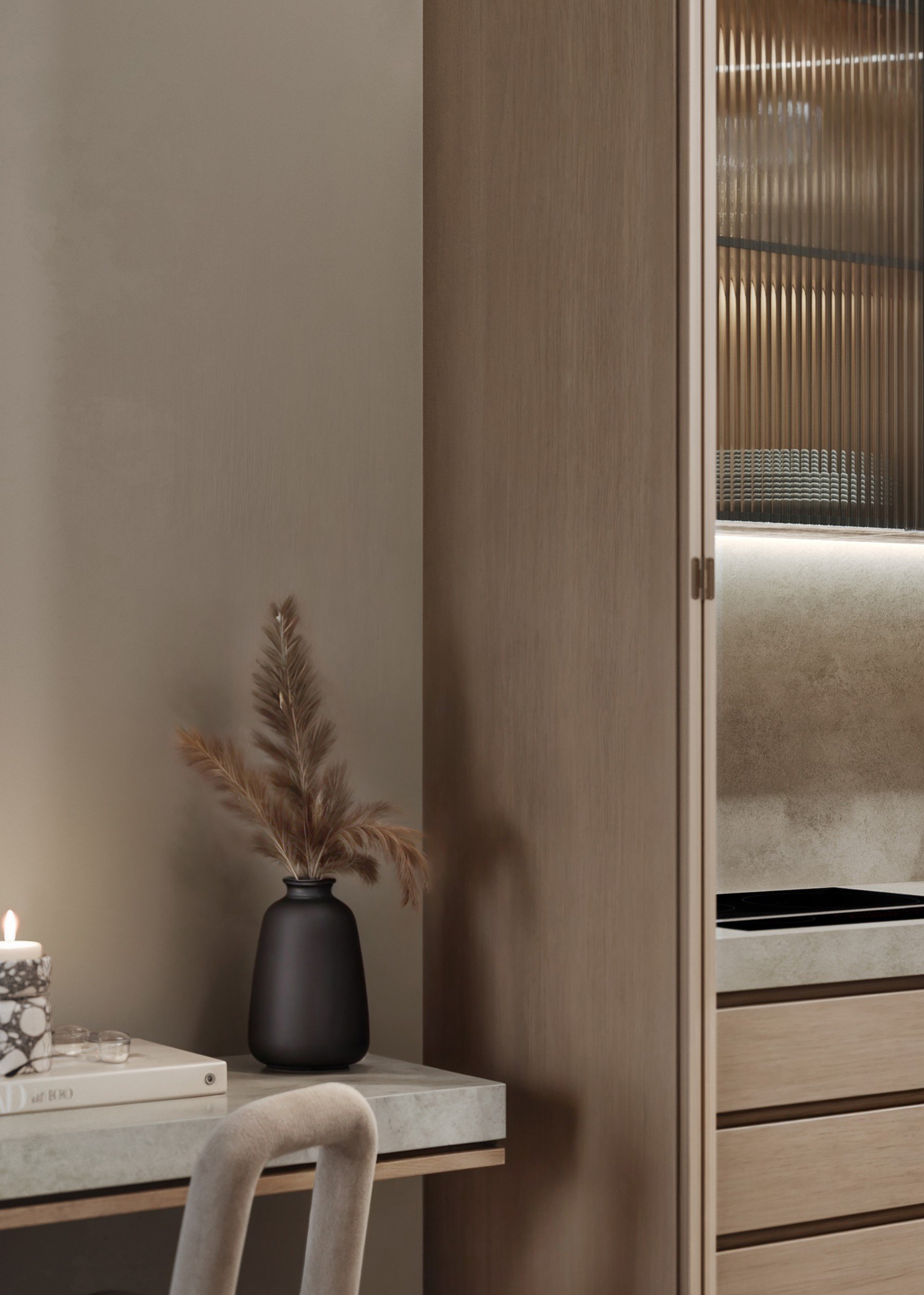 A corner of a room with a black vase holding dried pampas grass, a marble tray with small candles, a beige upholstered chair, and a wooden cabinet with a textured glass door.