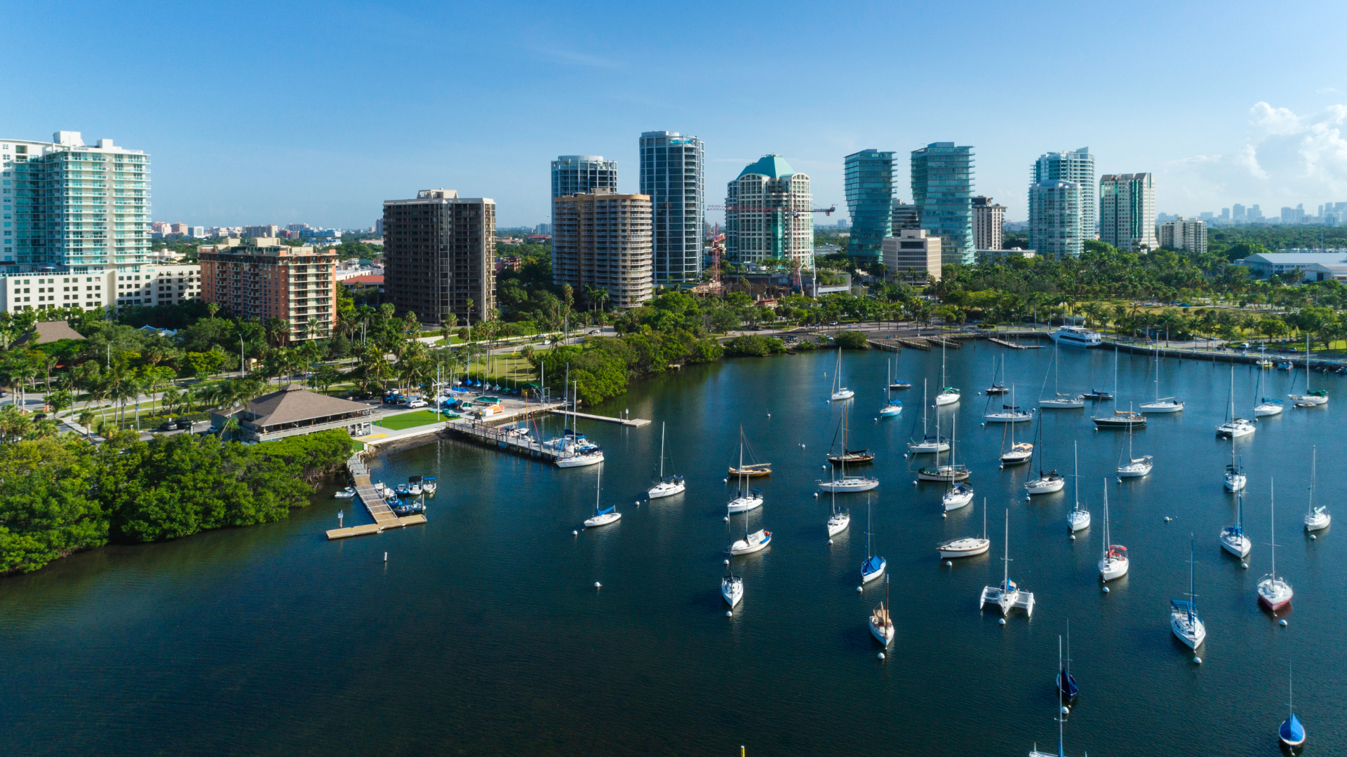 Coconut Grove skyline with high-rise buildings and a marina with numerous sailboats and yachts on calm water.