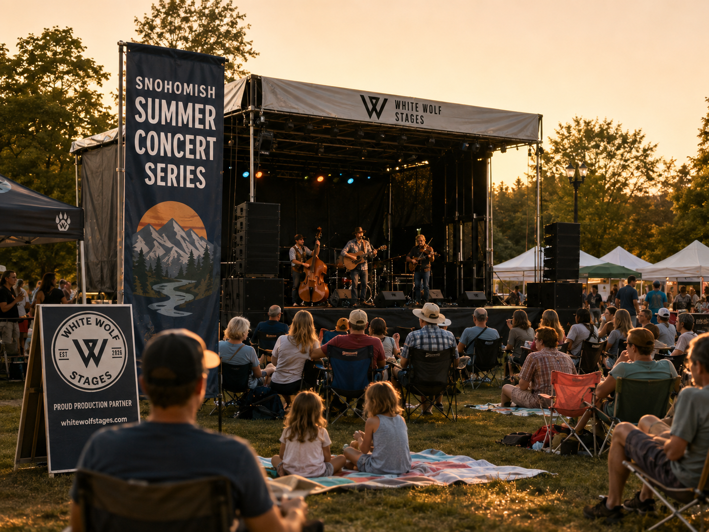 People watching a live band perform on an outdoor stage at sunset during the Snohomish Summer Concert Series, with tents and trees in the background.