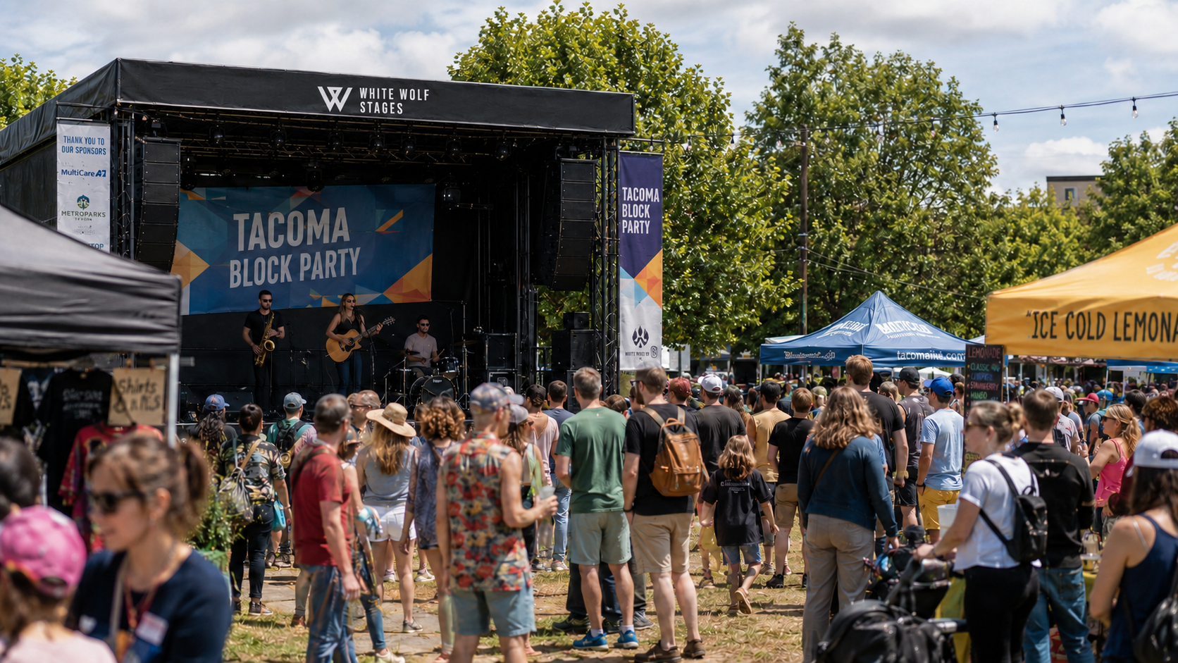 People attending the Tacoma Block Party with a band performing on an outdoor stage named White Wolf Stages, surrounded by tents and trees.