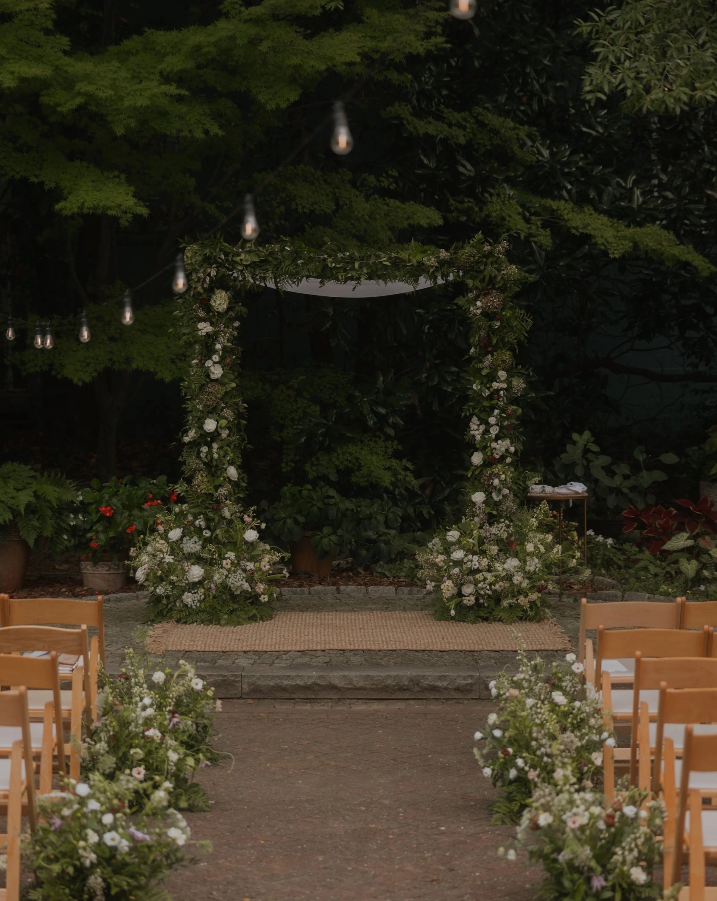 Wedding altar decorated with flowers and greenery, set outdoors with chairs arranged on either side.