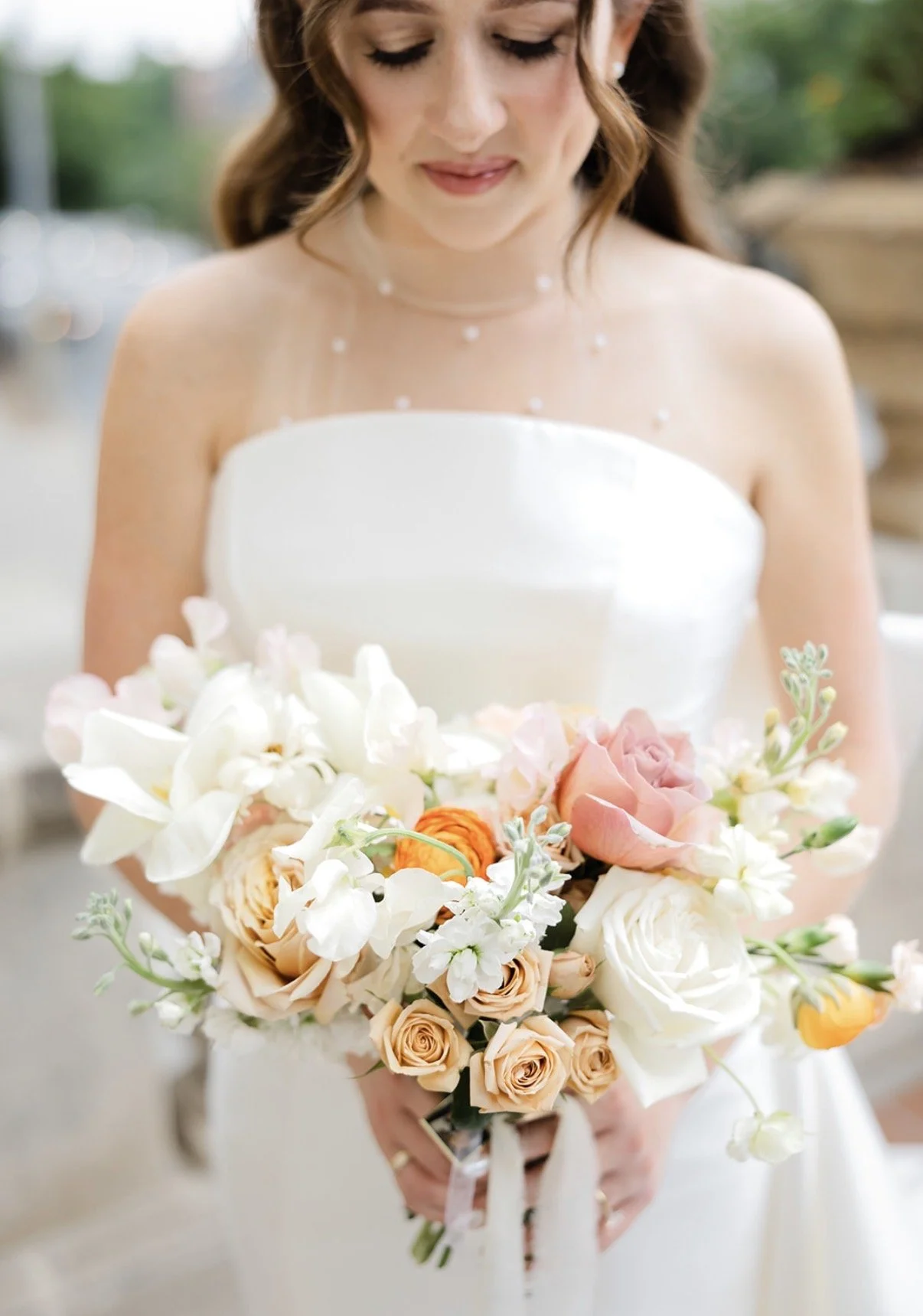 A bride in a strapless white wedding gown holding a large bouquet of white, blush, and peach-colored flowers.