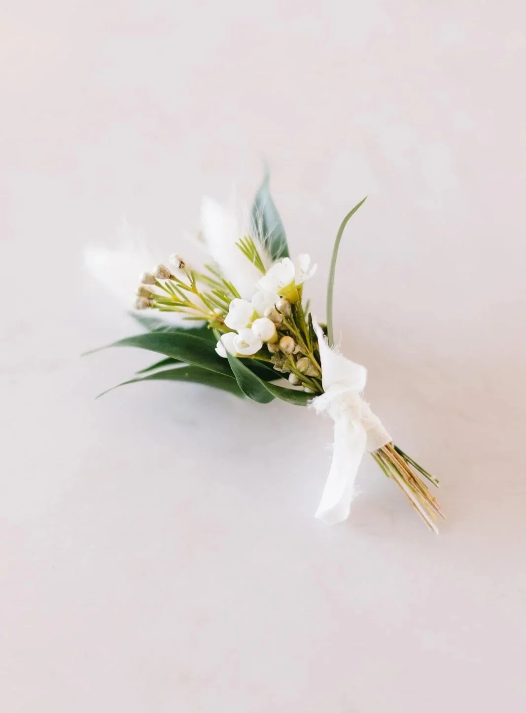Small bouquet of white flowers and green leaves tied with white ribbon