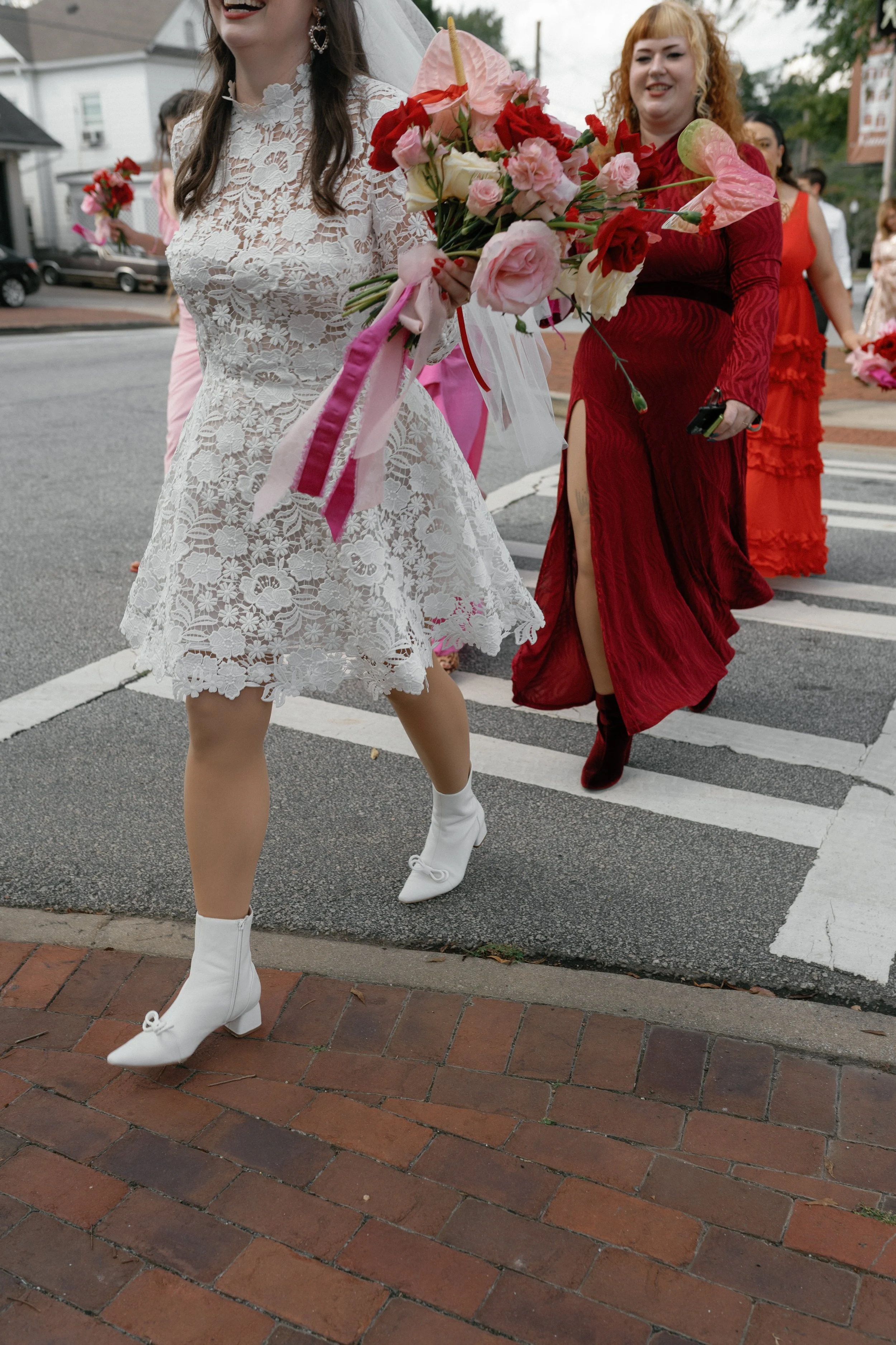 People walking in a wedding procession outdoors, holding bouquets of colorful flowers, wearing elegant dresses and high heels.