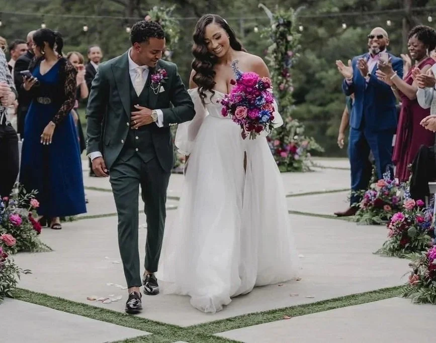 Bride and groom walking down the aisle at their outdoor wedding, surrounded by friends and family, with flowers and greenery in the background.