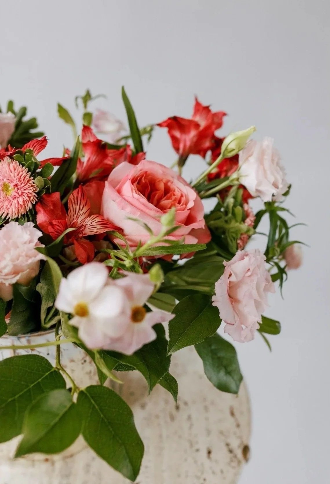 A bouquet of pink, white, and red flowers in a white vase against a plain background.