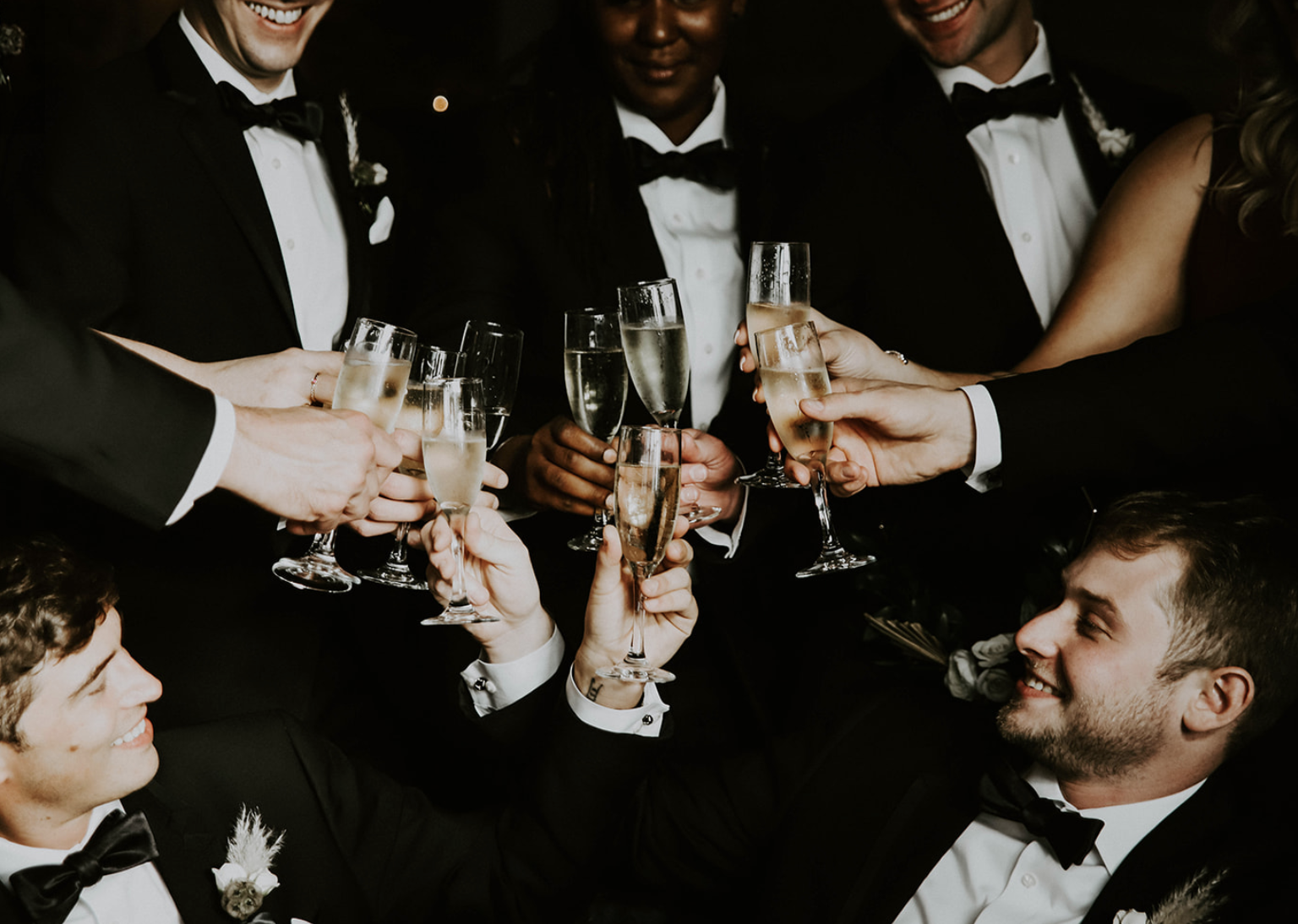 Group of people in tuxedos and evening dresses toasting with champagne glasses at a celebration.