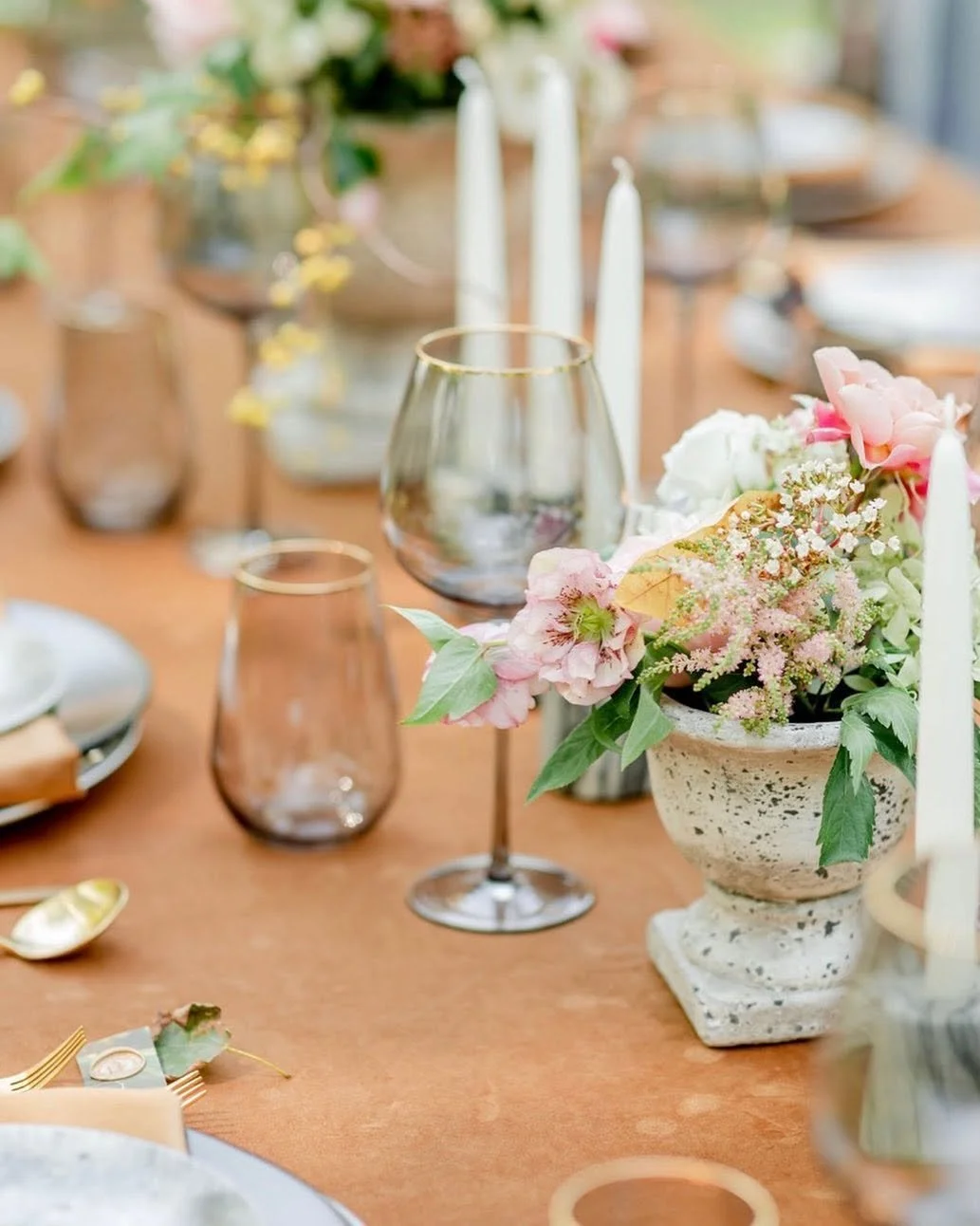 Elegant table setting with flower centerpiece, wine glasses, candles, and tableware on a wooden table.
