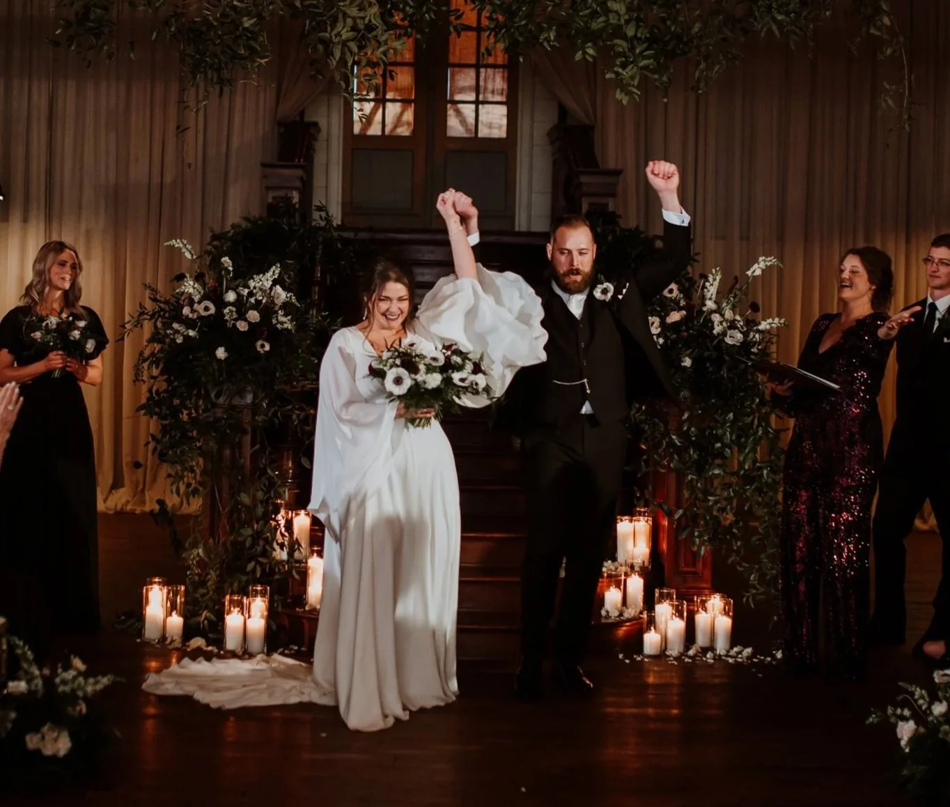 Wedding ceremony with a bride and groom celebrating, surrounded by bridesmaids and groomsmen, with candles and floral decorations.