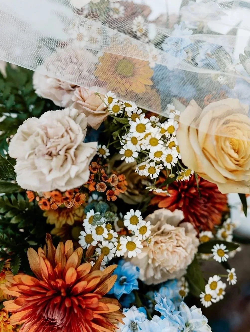 A colorful bouquet of various flowers, including daisies, roses, chrysanthemums, and other blossoms with green foliage, arranged in a container.
