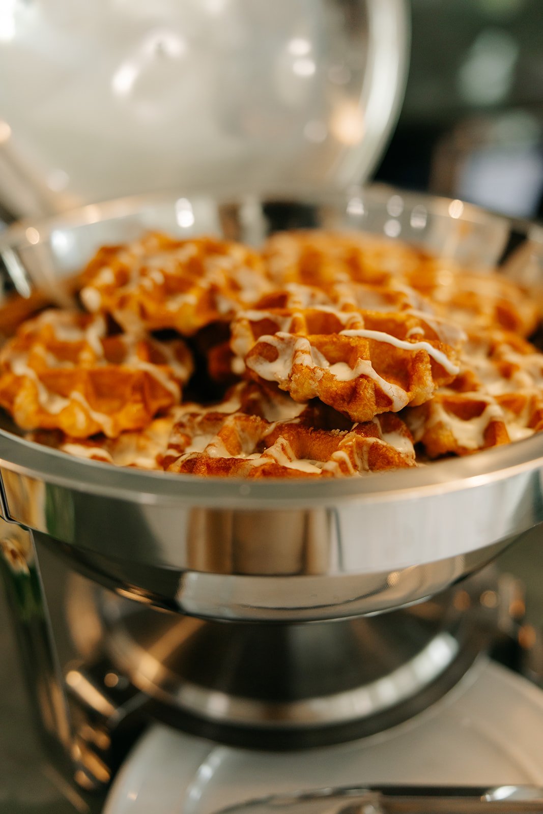 Waffles with white icing in a metal chafing dish.